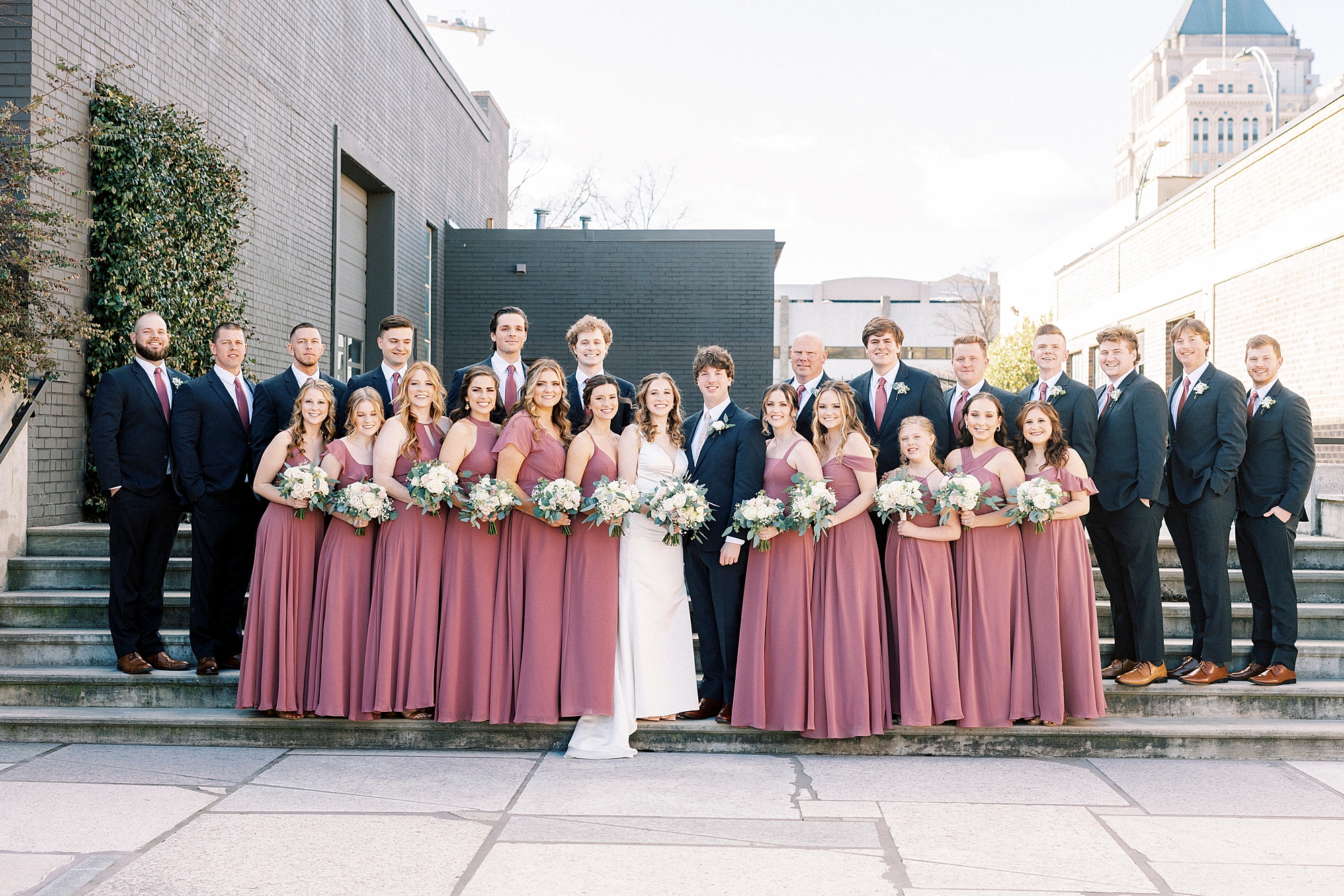 bride and groom pose with large wedding party on steps of the Cadillac Service Garage