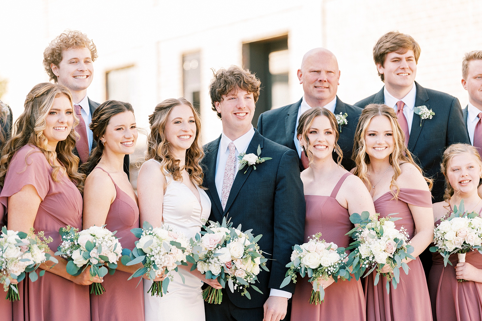 bridesmaids in pink and groomsmen in navy stand around couple on steps at Cadillac Service Garage