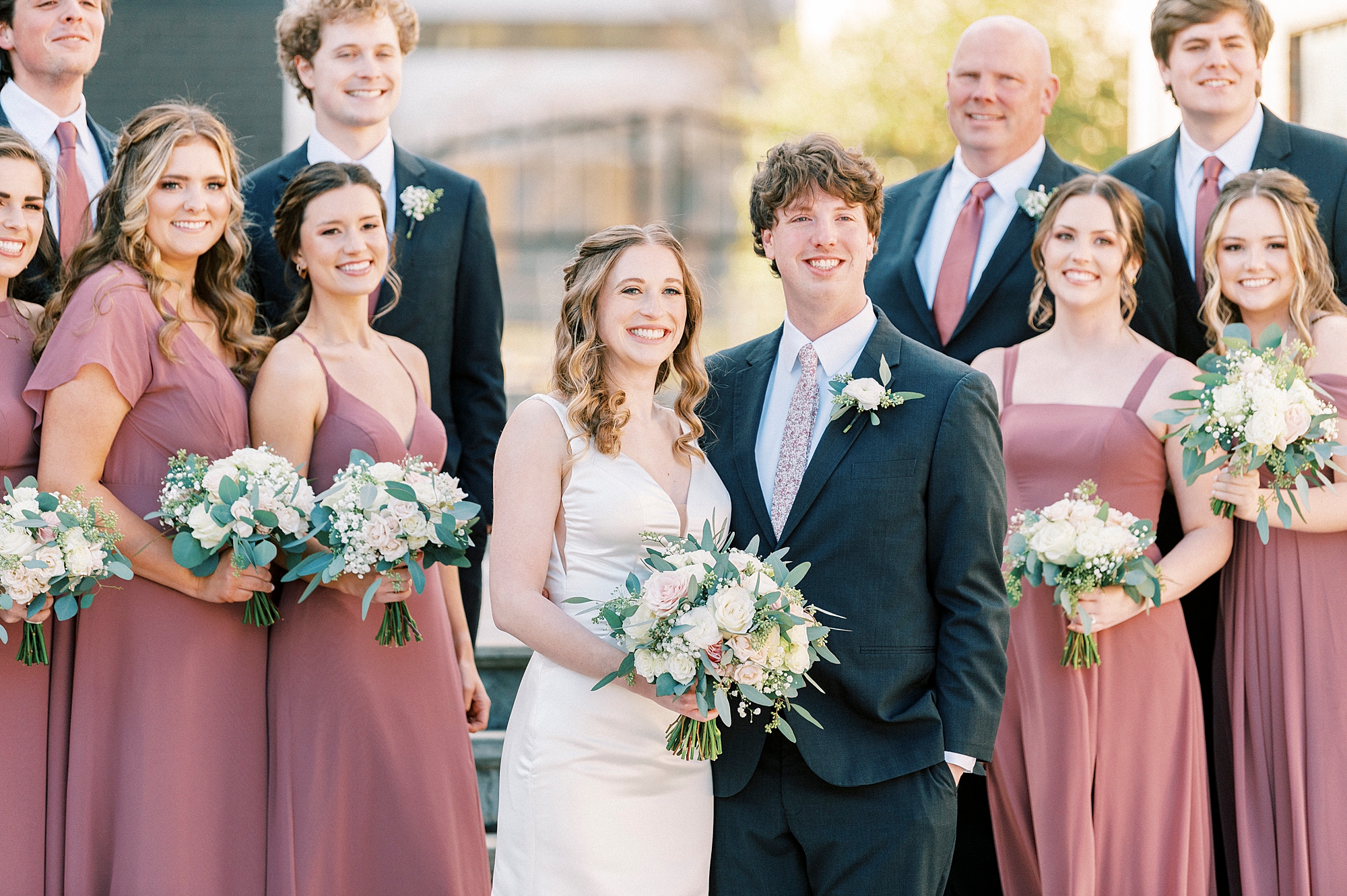 newlyweds smile with wedding party next to them at the Cadillac Service Garage