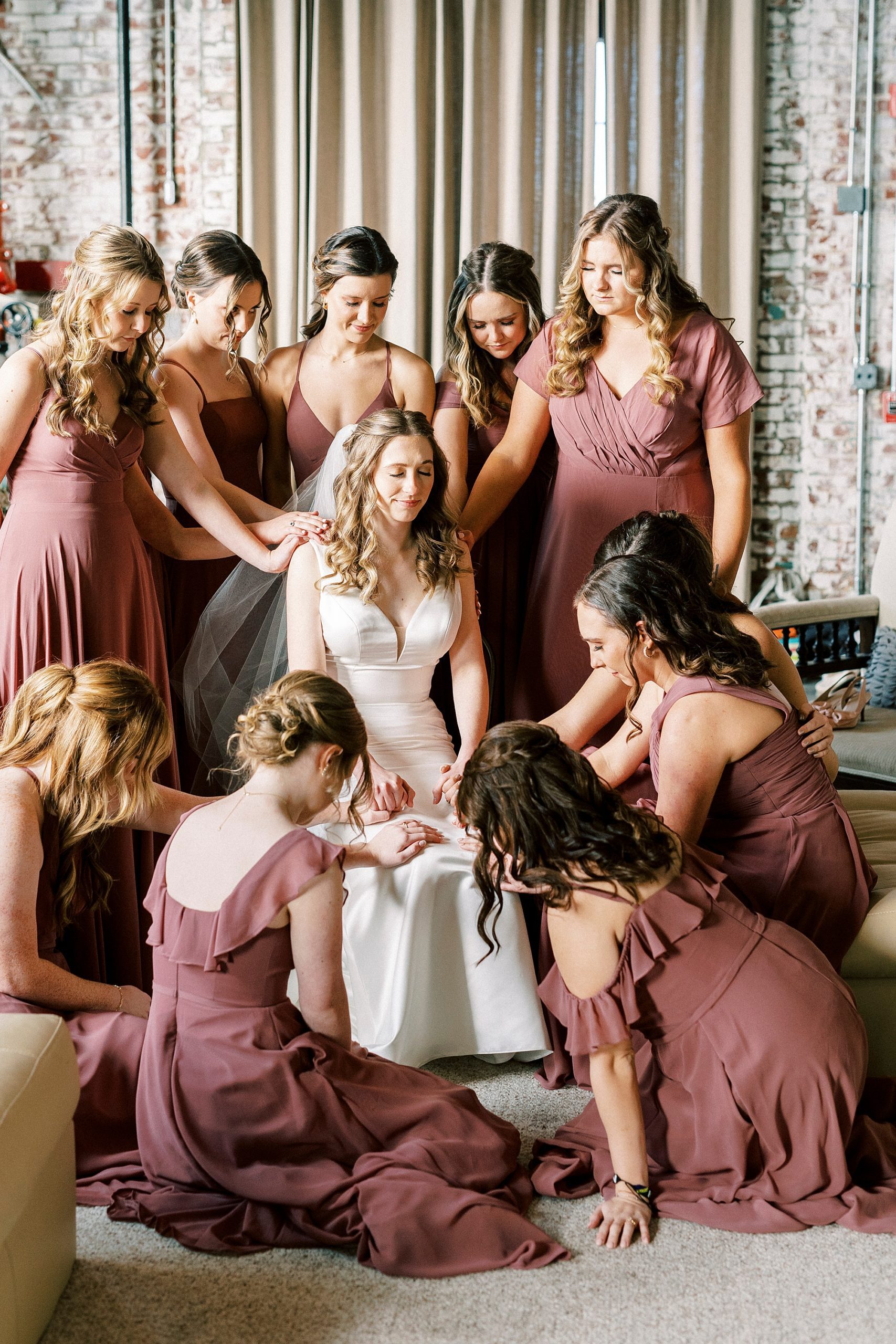 bridesmaids touch bride praying with her on wedding day 