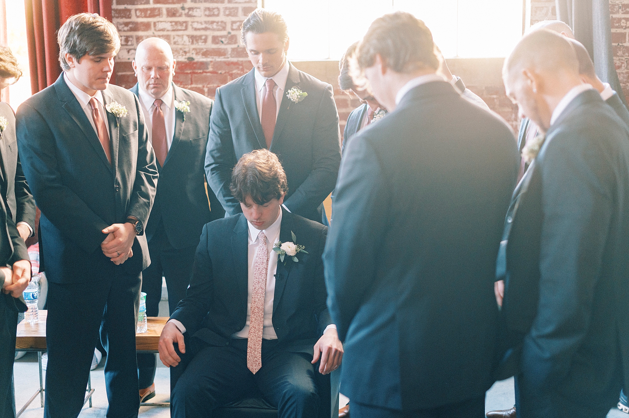 groomsmen pray around groom before ceremony 