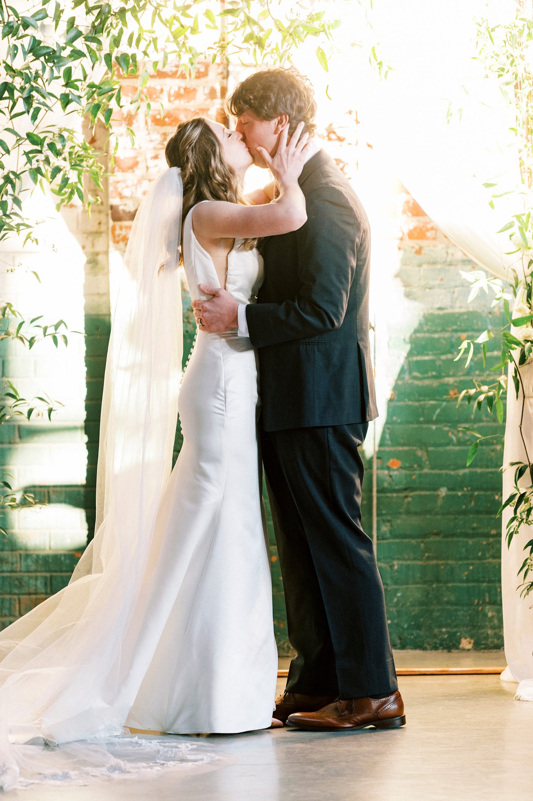 bride and groom kiss by alter during Christ-centered wedding ceremony at the Cadillac Service Garage in Greensboro NC