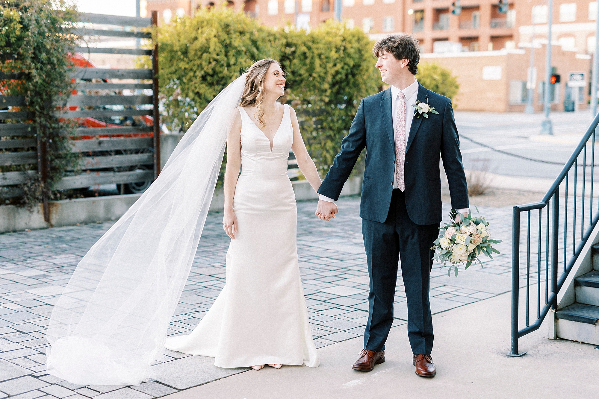 newlyweds smile and laugh walking across patio at the Cadillac Service Garage
