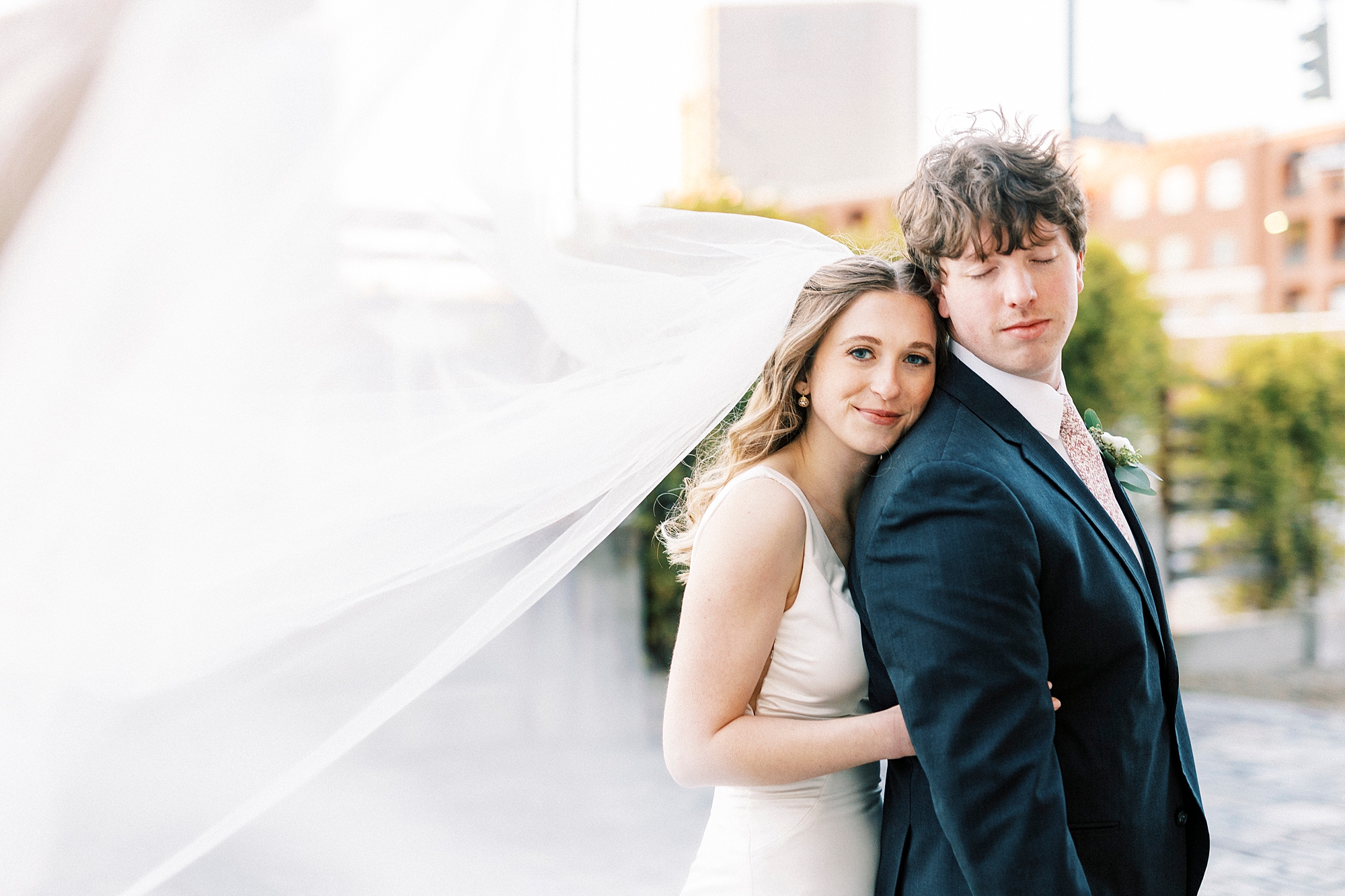 bride hugs groom from behind with veil floating behind them 