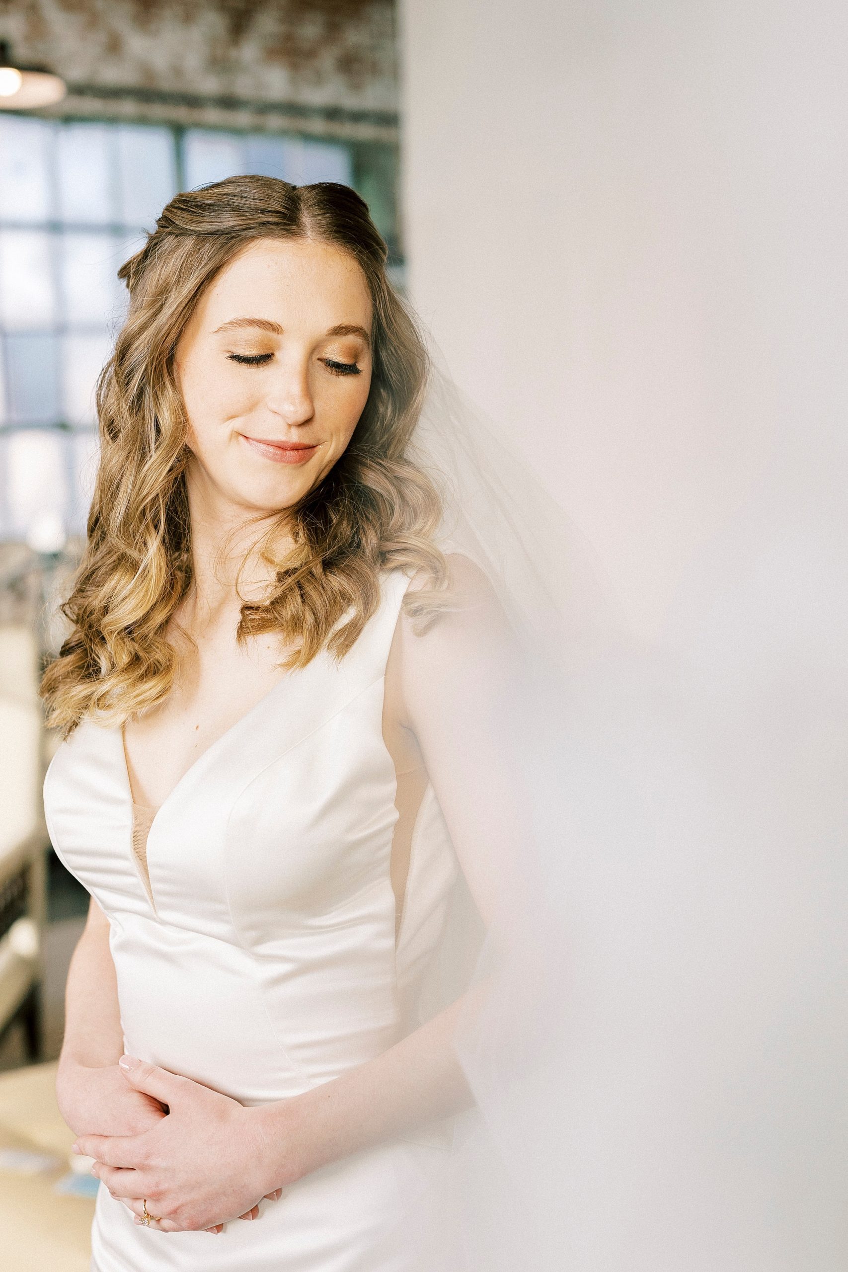 bride smiles looking over shoulder with veil around them 