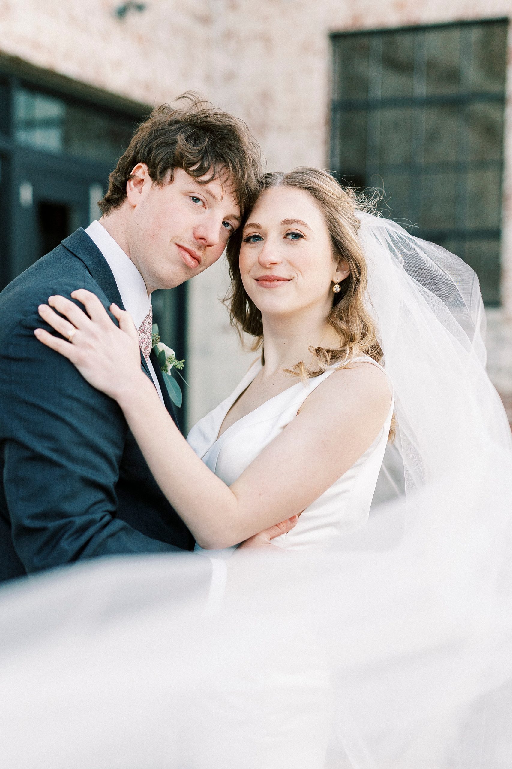 bride and groom hug with veil wrapped around them 