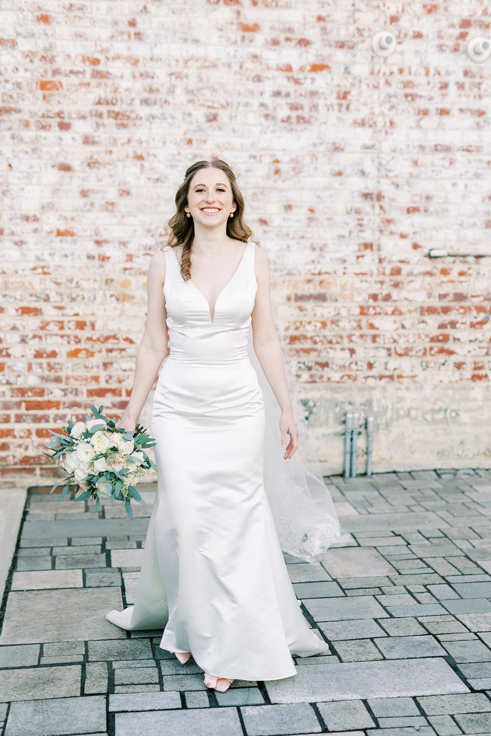 bride walks away from brick wall with bouquet by her side 