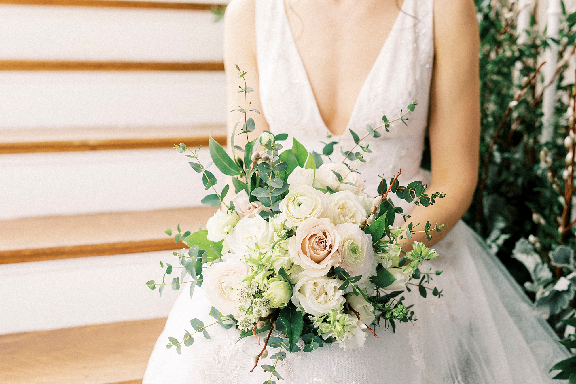 bride sits on steps holding bouquet of pastel pink and ivory flowers 