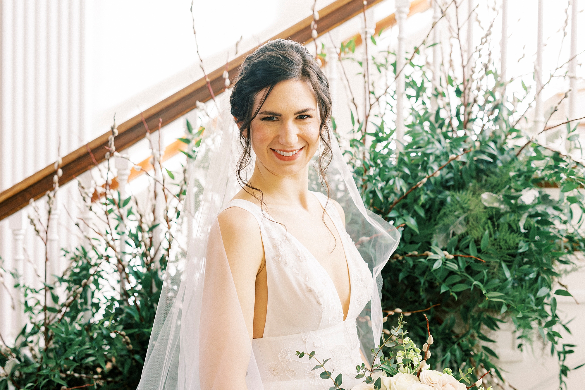 bride smiles with veil around shoulders in front of greenery on staircase at Separk Mansion