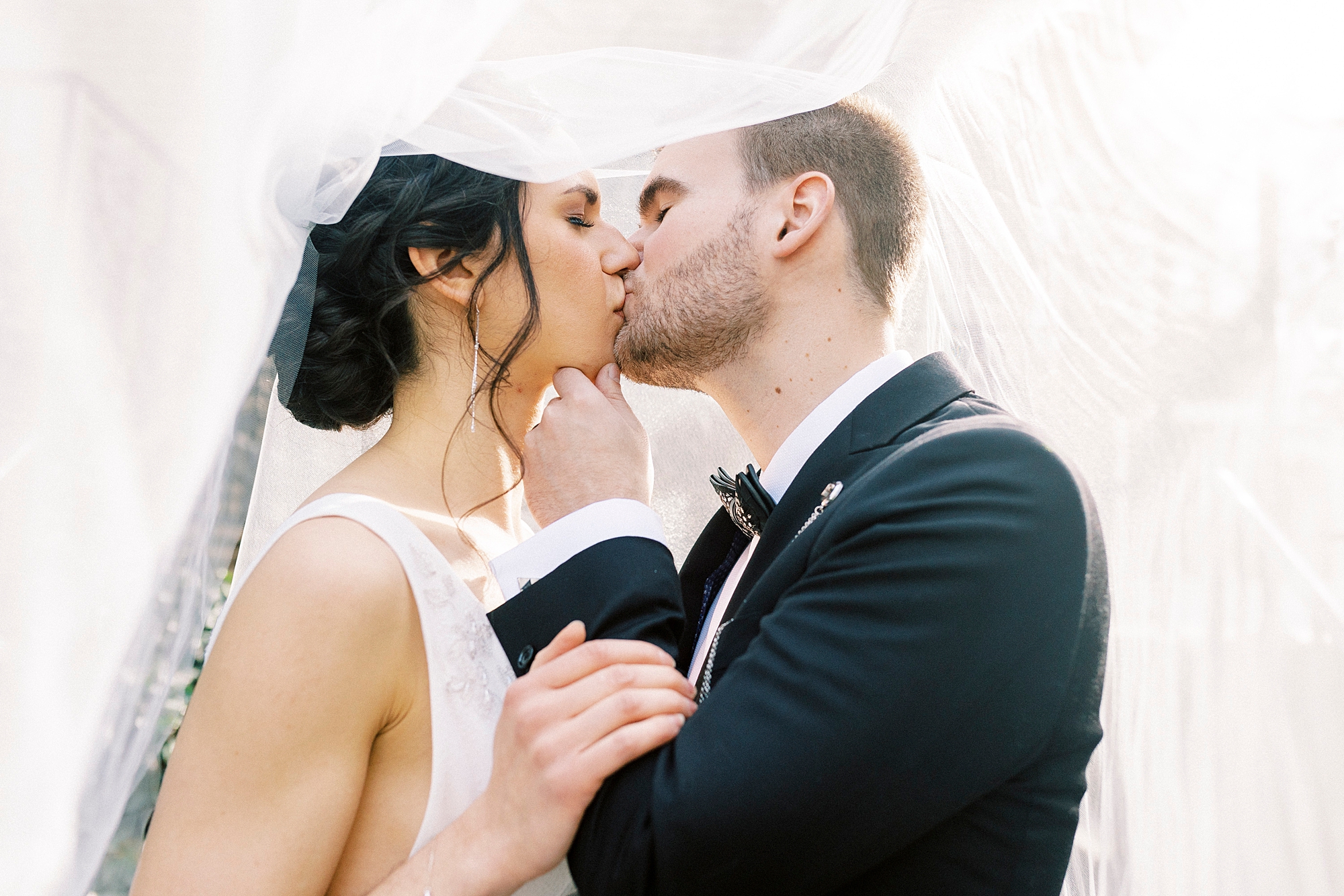 bride and groom kiss under wedding veil 