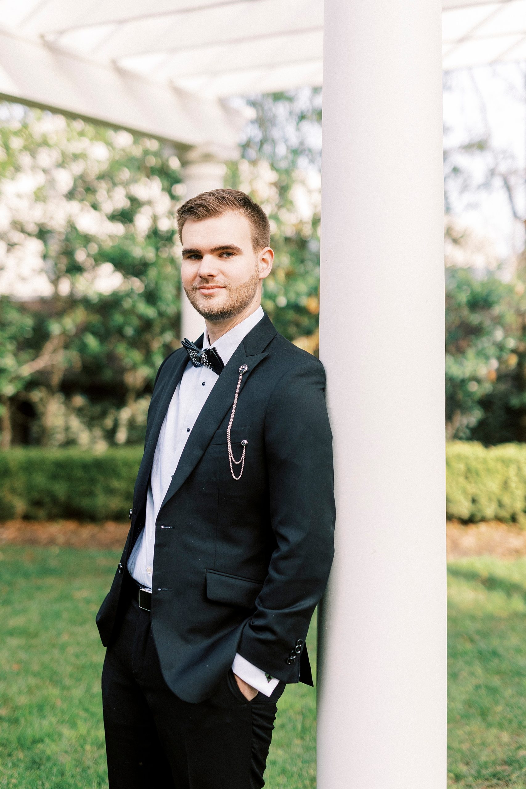 groom in tux leans against white pillar at Separk Mansion