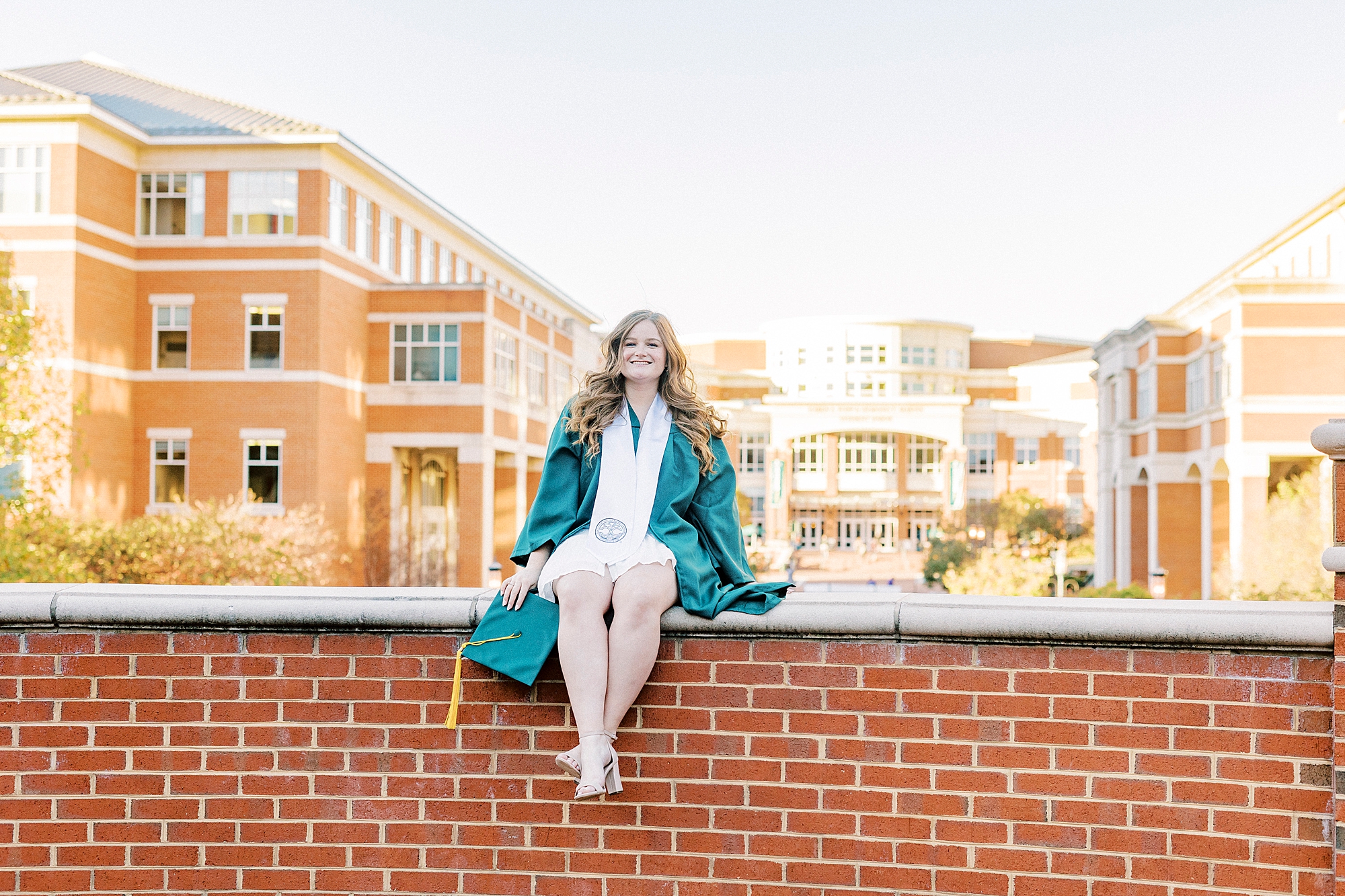 college senior sits on brick wall during UNC Charlotte senior portraits