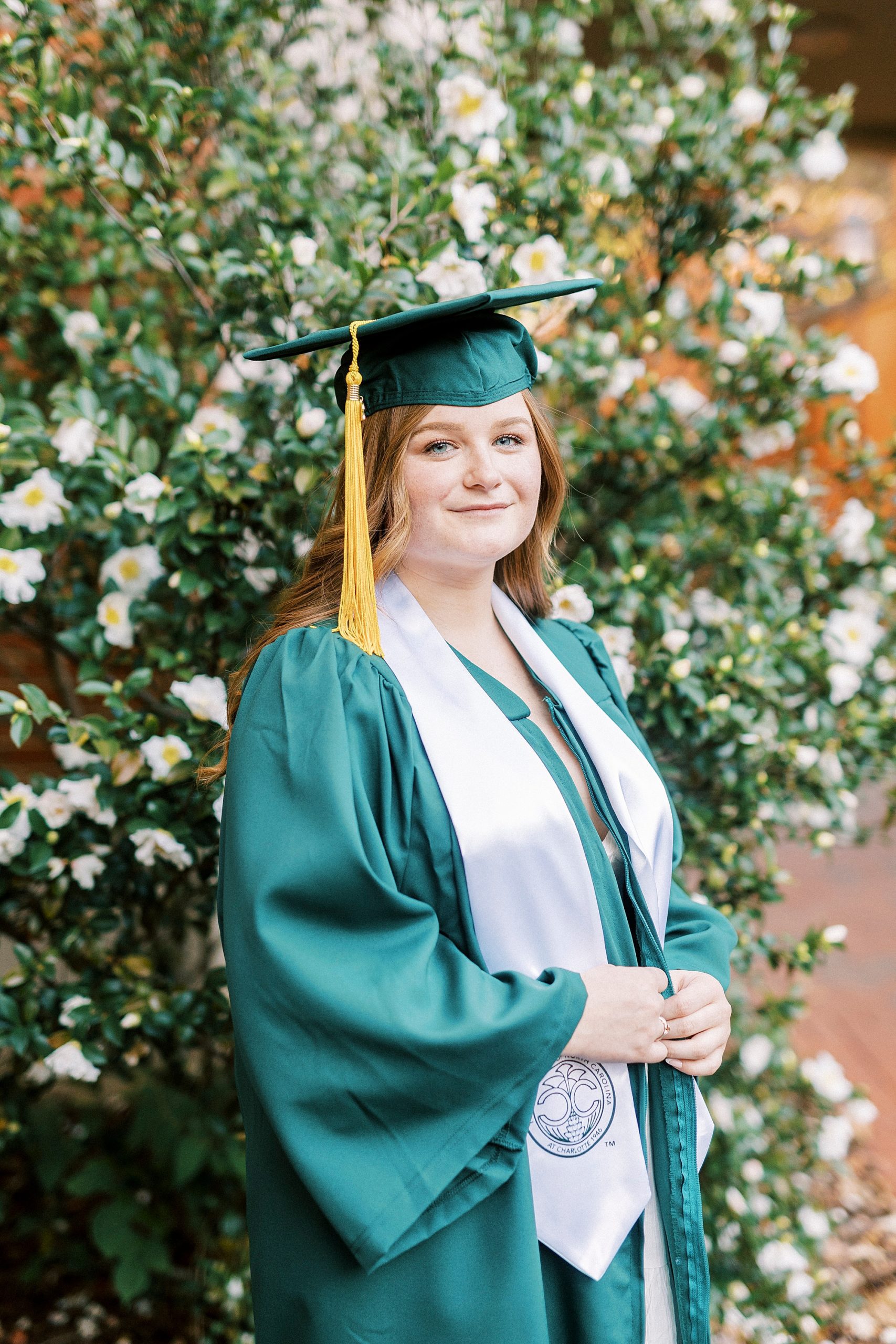 woman poses in green cap and gown during UNC Charlotte senior portraits