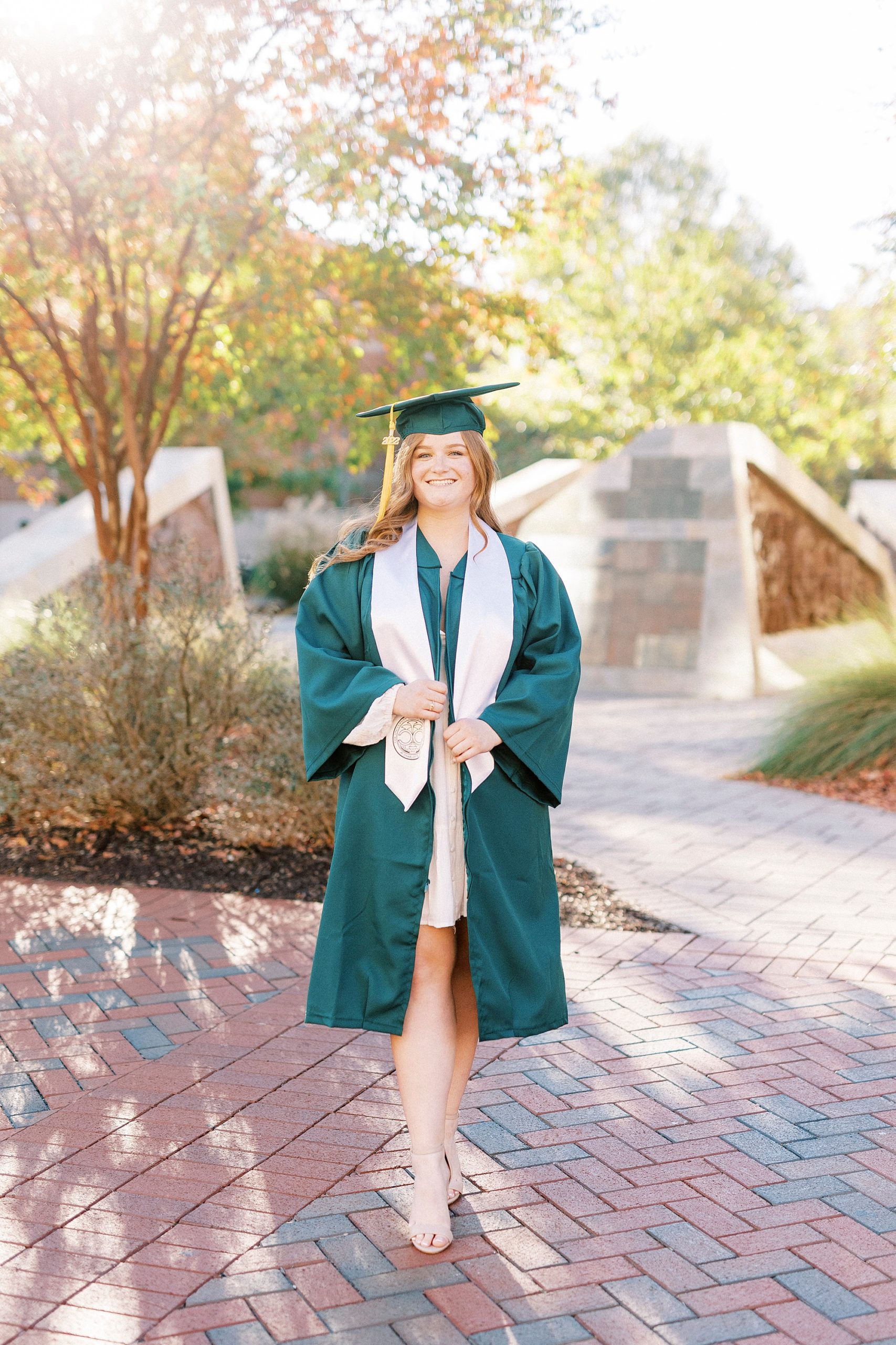 graduate stands on brick patio during UNC Charlotte senior portraits