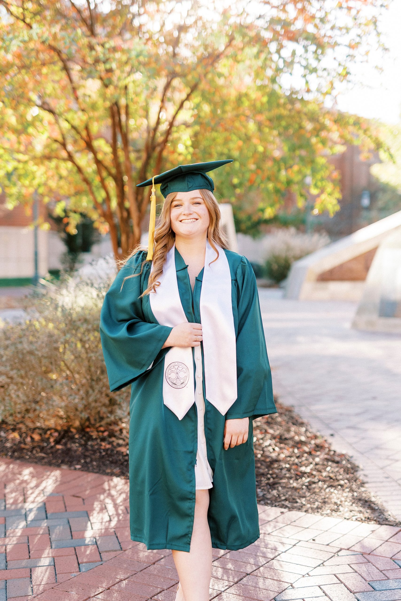 woman poses in green cap and gown with white stole
