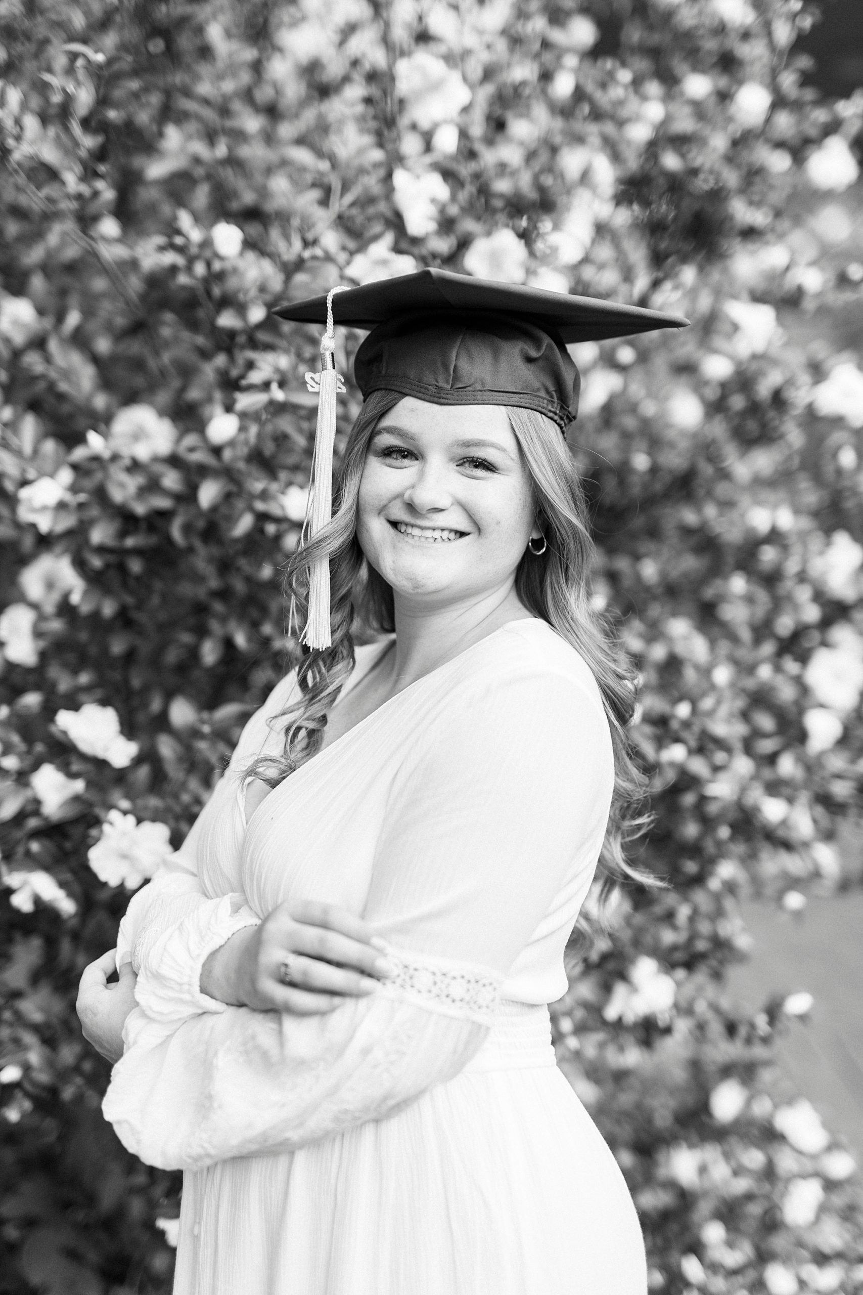 woman poses in white dress with cap during senior portraits
