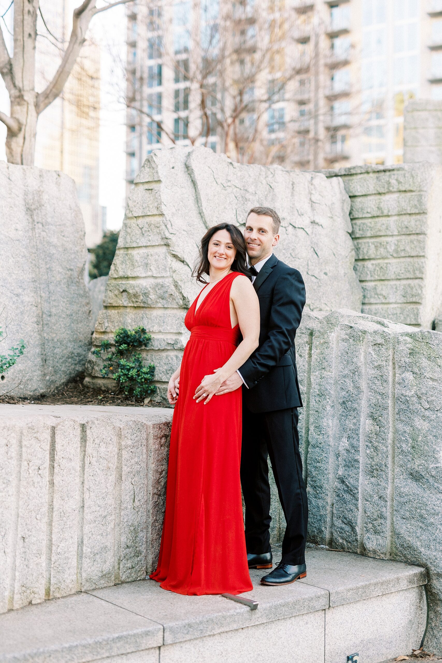 engaged couple hugs in classy attire by fountain in Romare Bearden Park