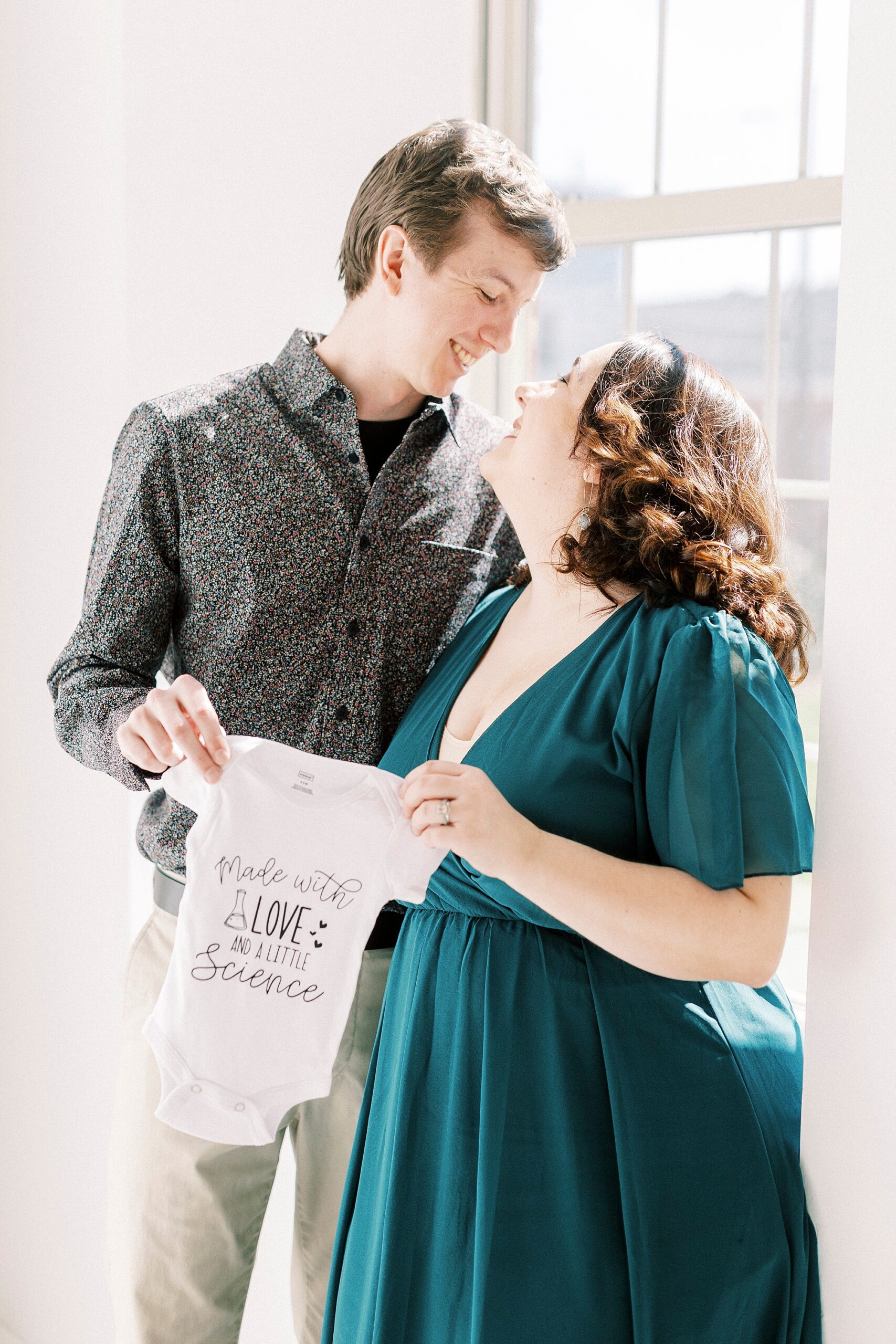 couple smiles at each other during studio pregnancy announcement in Concord NC