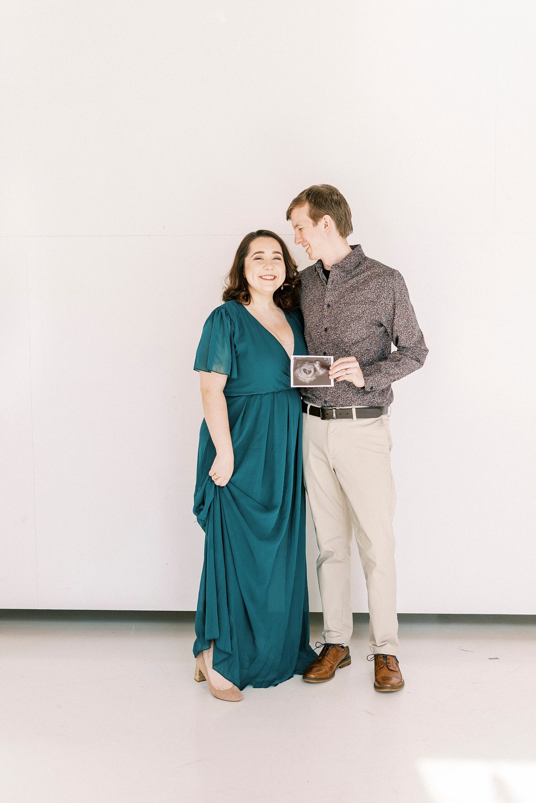 husband hugs wife looking down at her holding sonogram