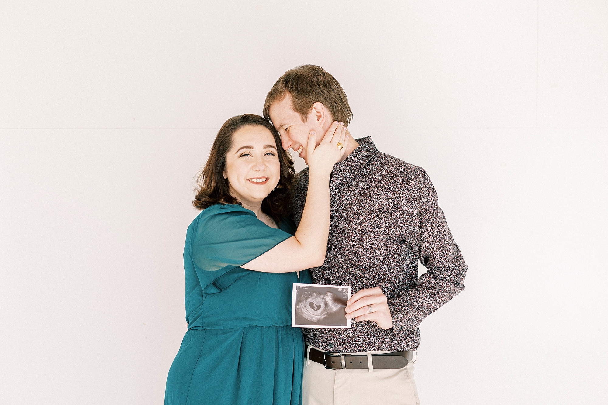 husband nuzzle wife's forehead during studio pregnancy announcement in Concord NC while holding sonogram