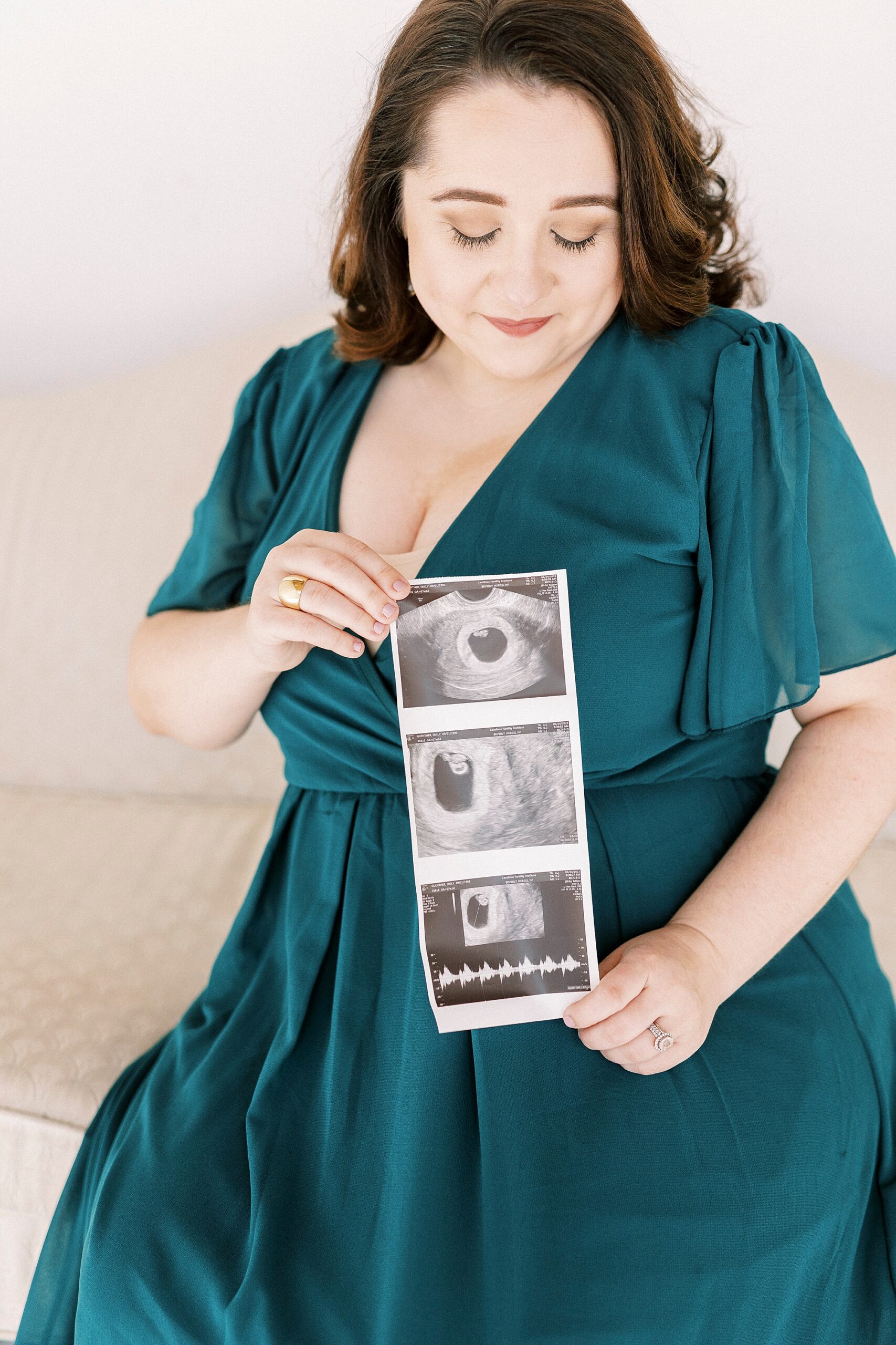 expecting mother holds sonogram in teal gown during studio pregnancy announcement in Concord NC