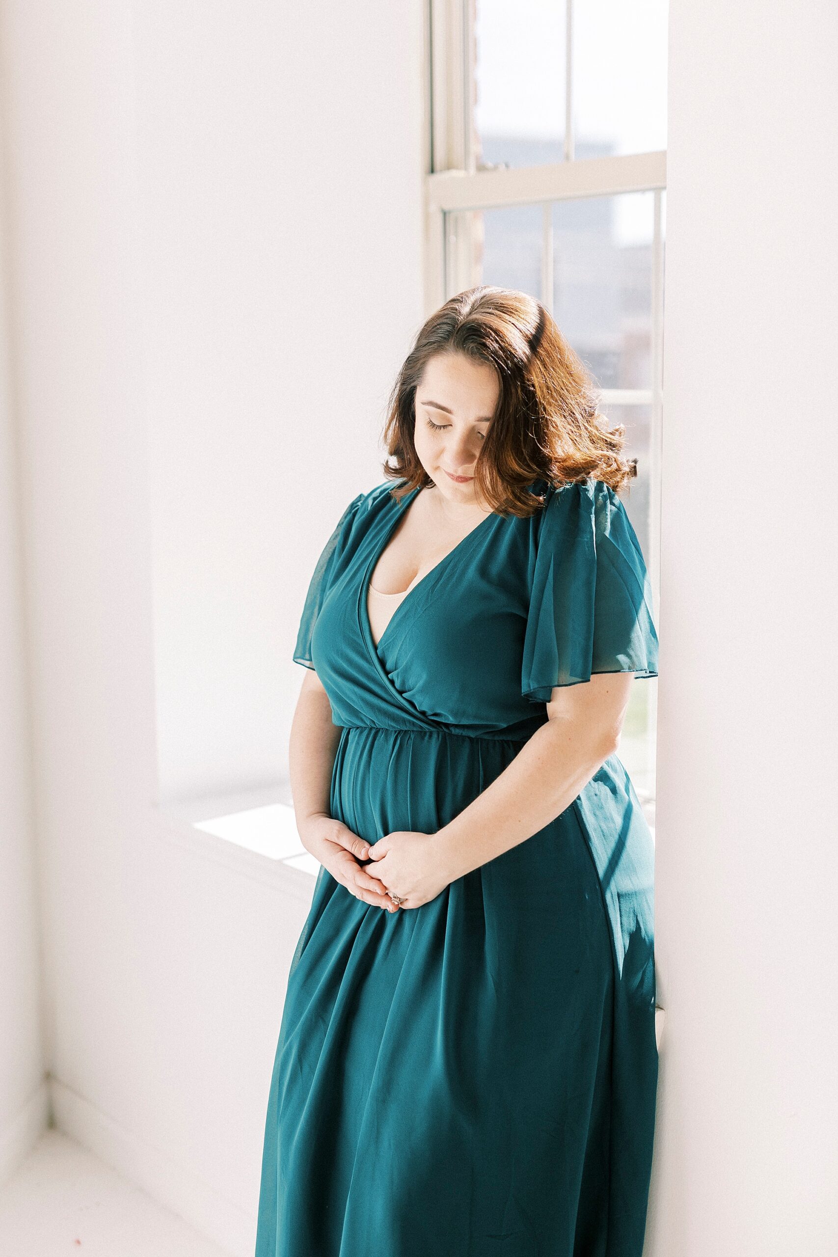 woman in teal gown holds baby bump looking down