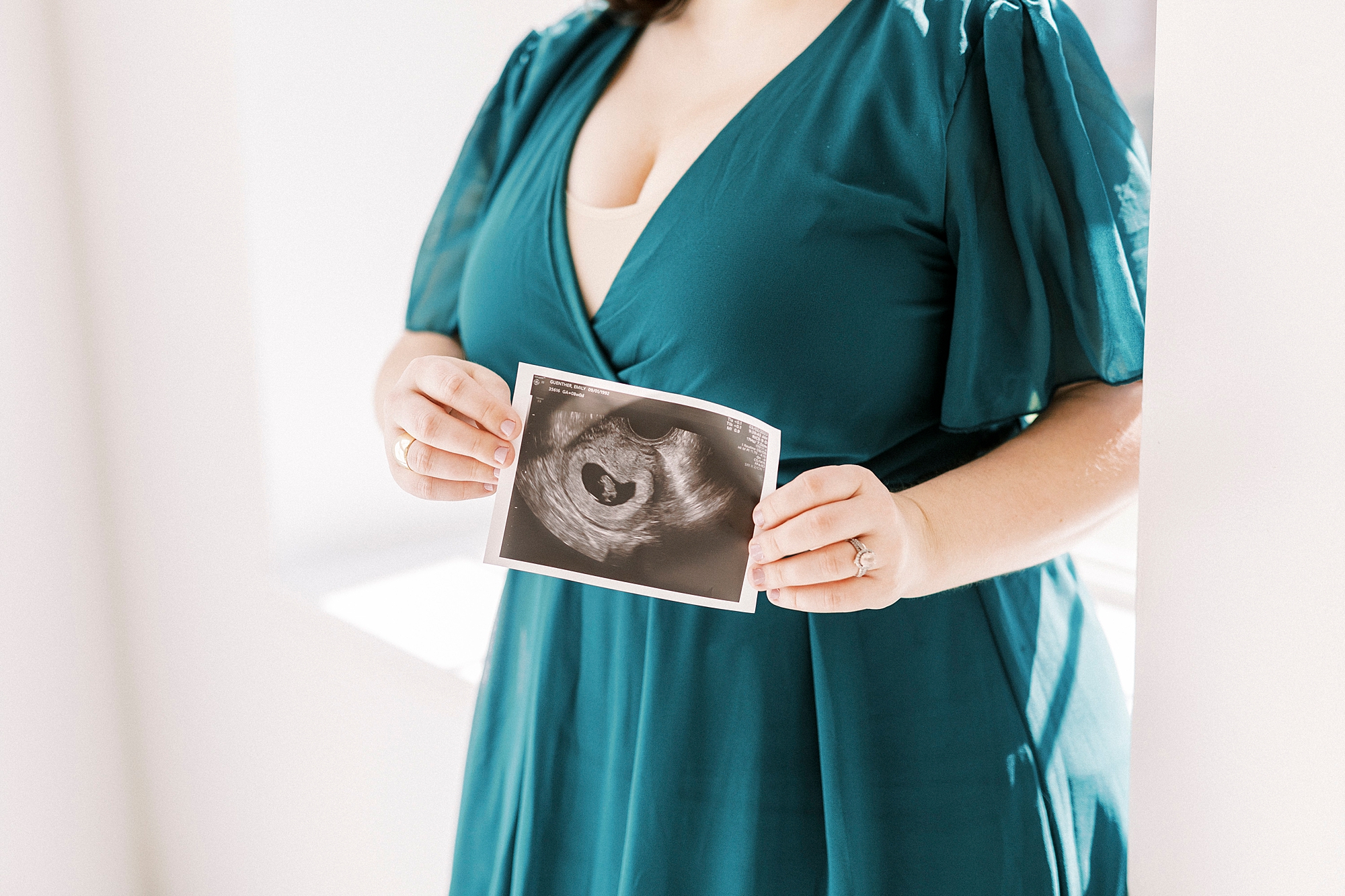expecting mother in teal gown holds sonogram photo during studio pregnancy announcement in Concord NC
