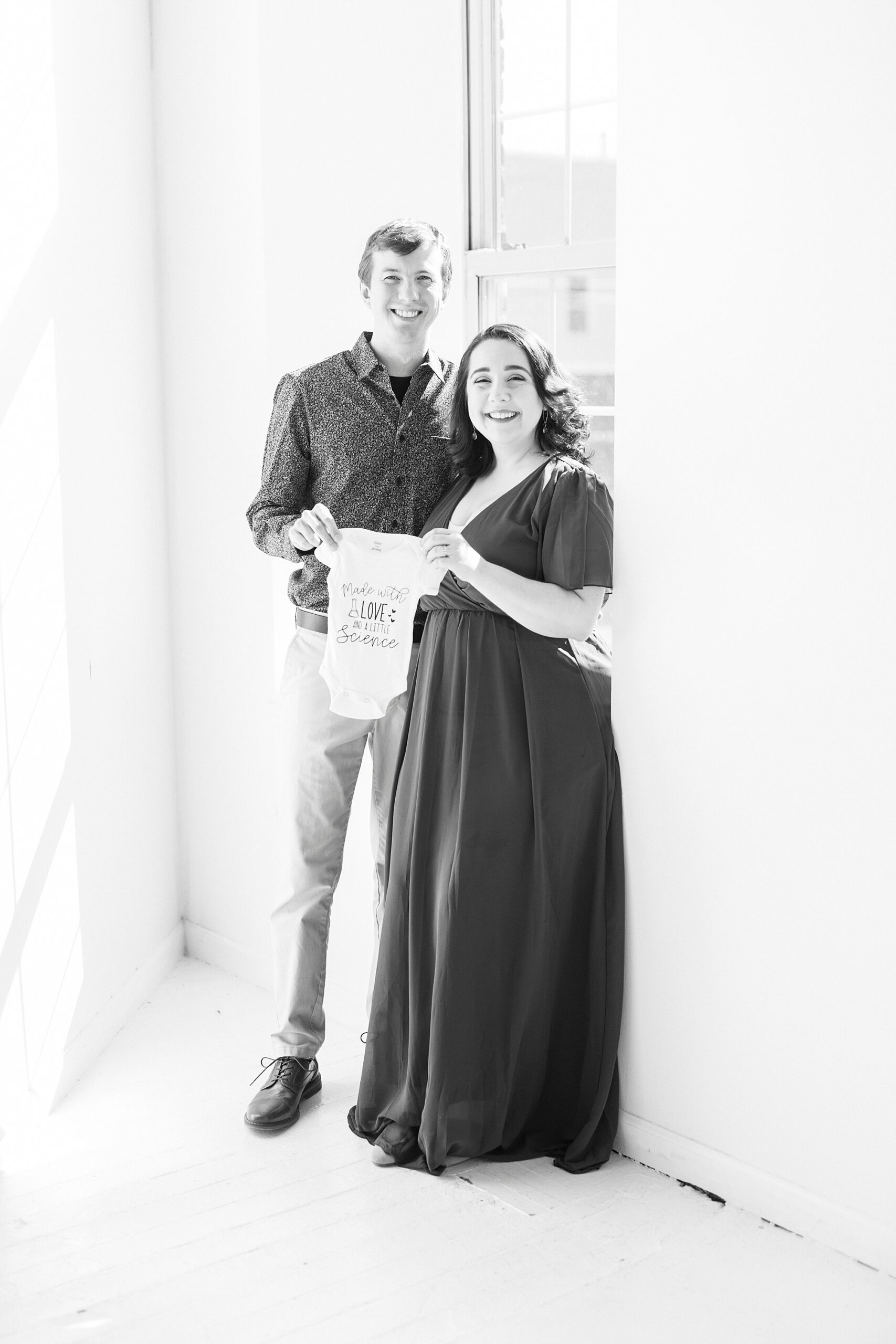married couple holds onesie in window at Concord NC studio