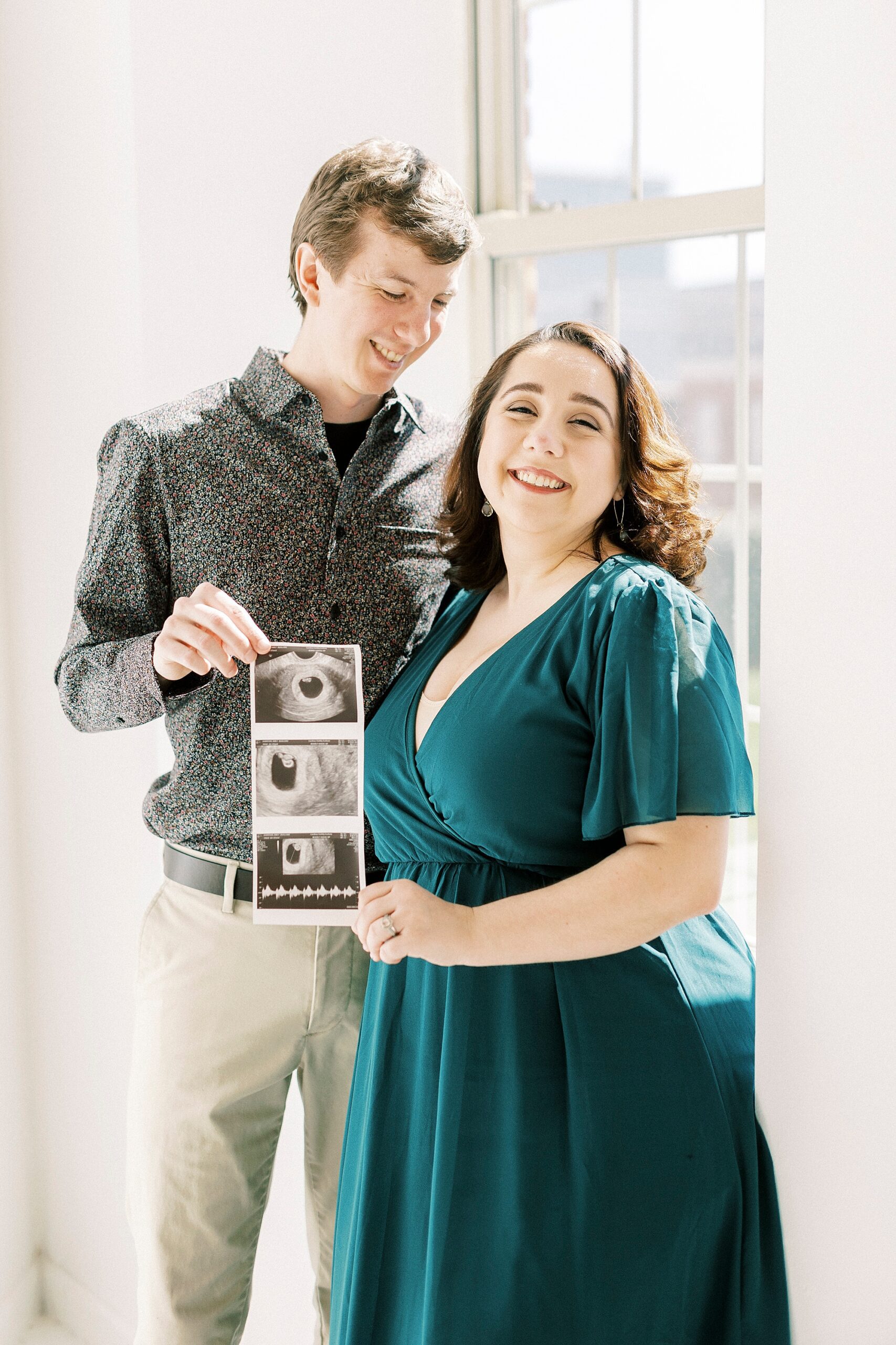 man looks down at wife while holding edge of sonogram photos