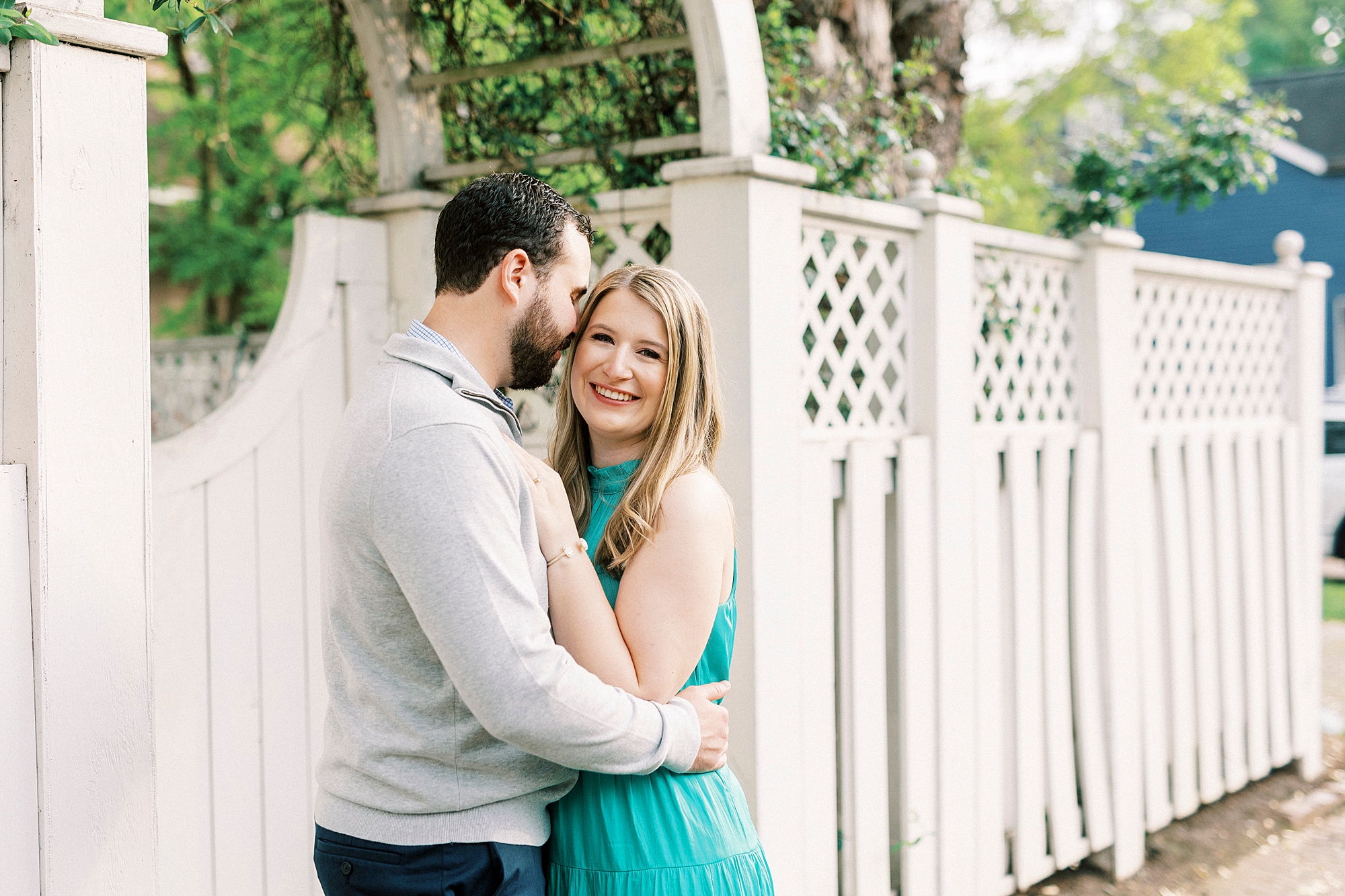 groom nuzzles bride's cheek near white fence at Fourth Ward Park