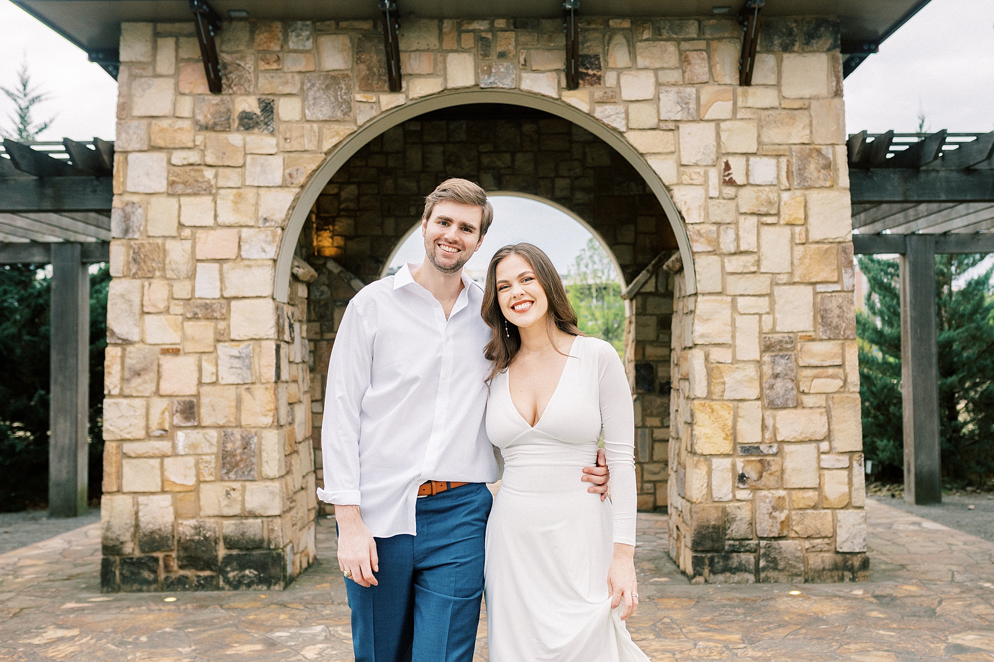 woman in white dress hugs fiancee under stone arbor at Midtown Park