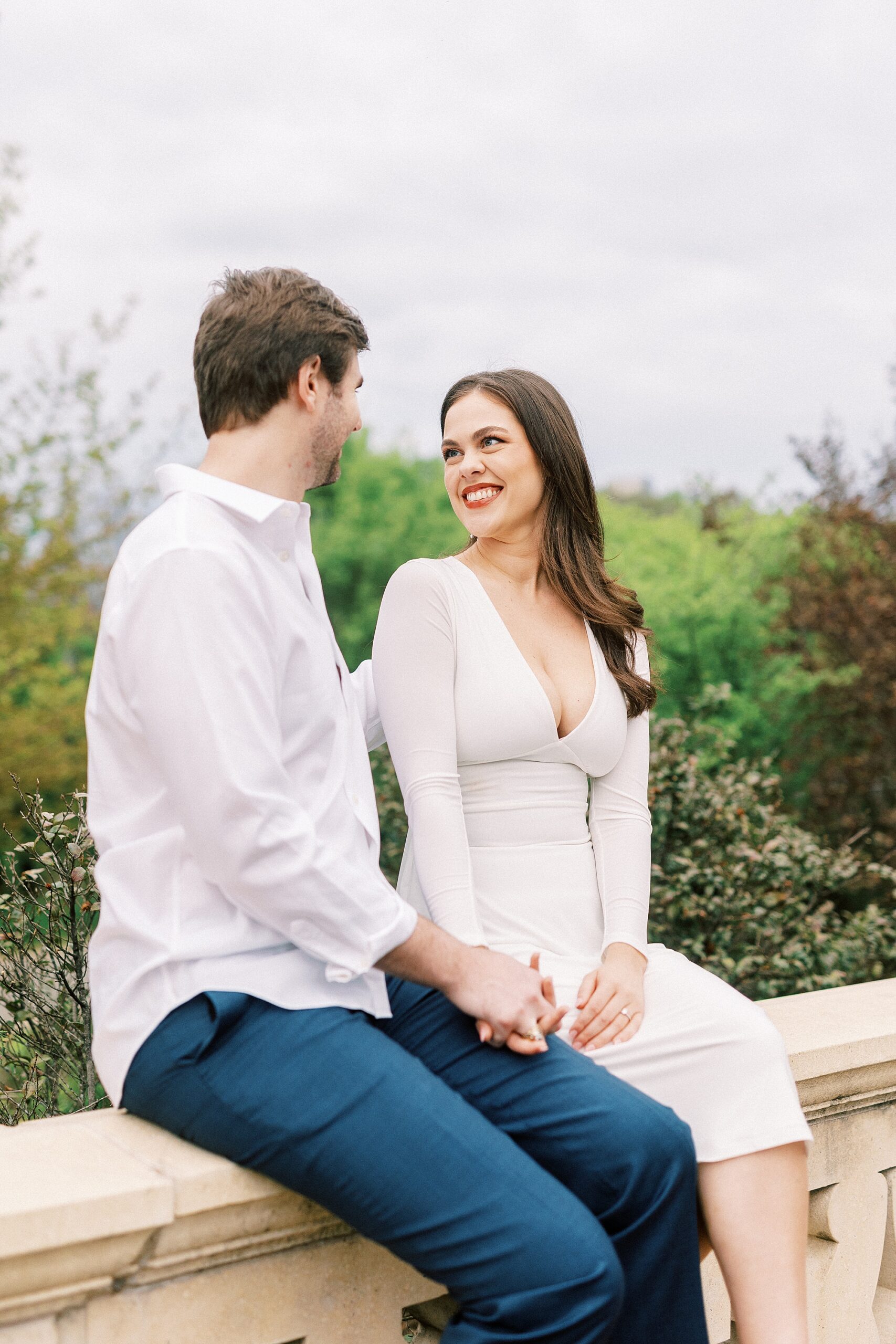 engaged couple sits on stone wall during Midtown Park engagement session 