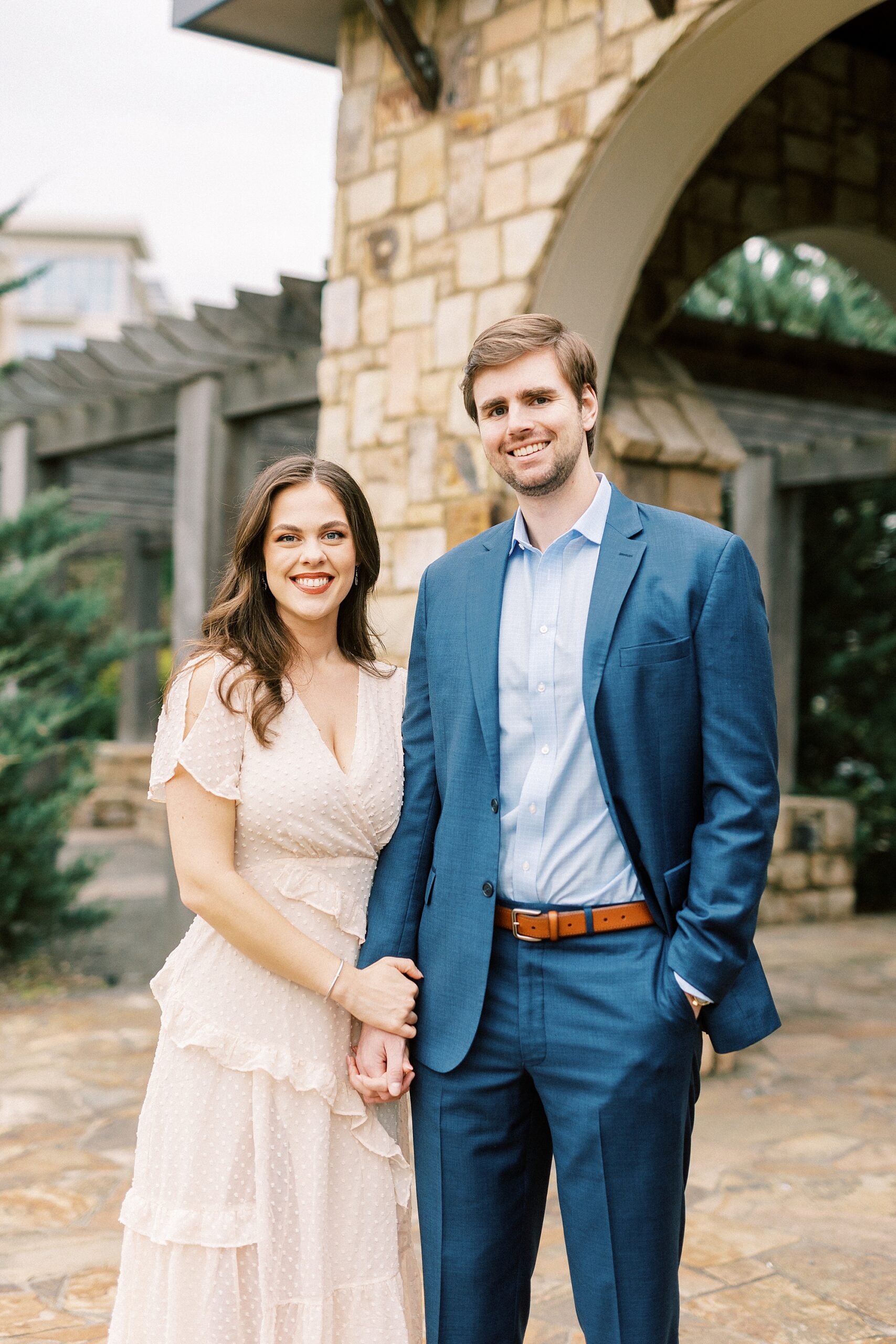 engaged couple holds hands in front of stone arch during Midtown Park engagement portraits