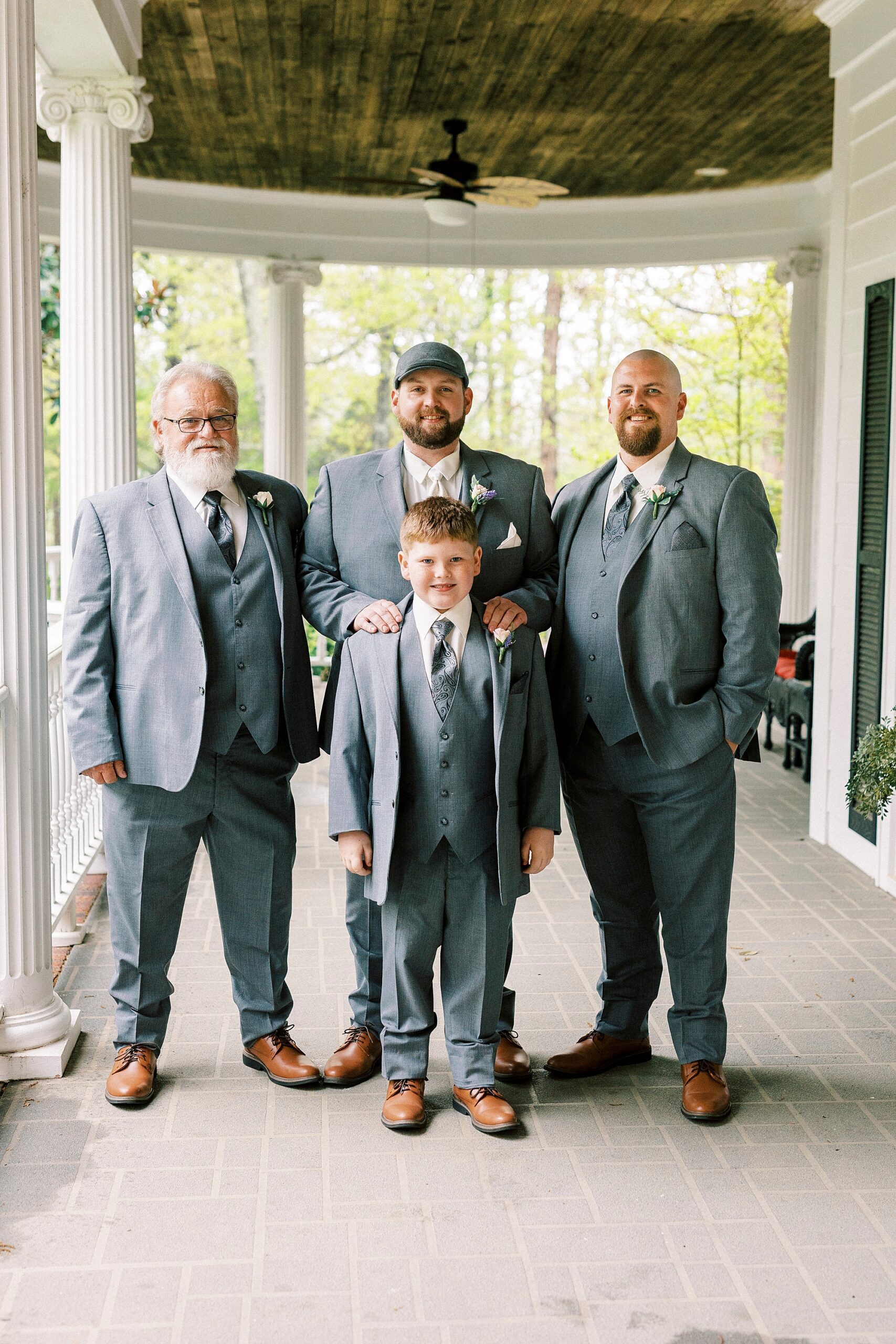 groom stands on patio with family in grey suits 