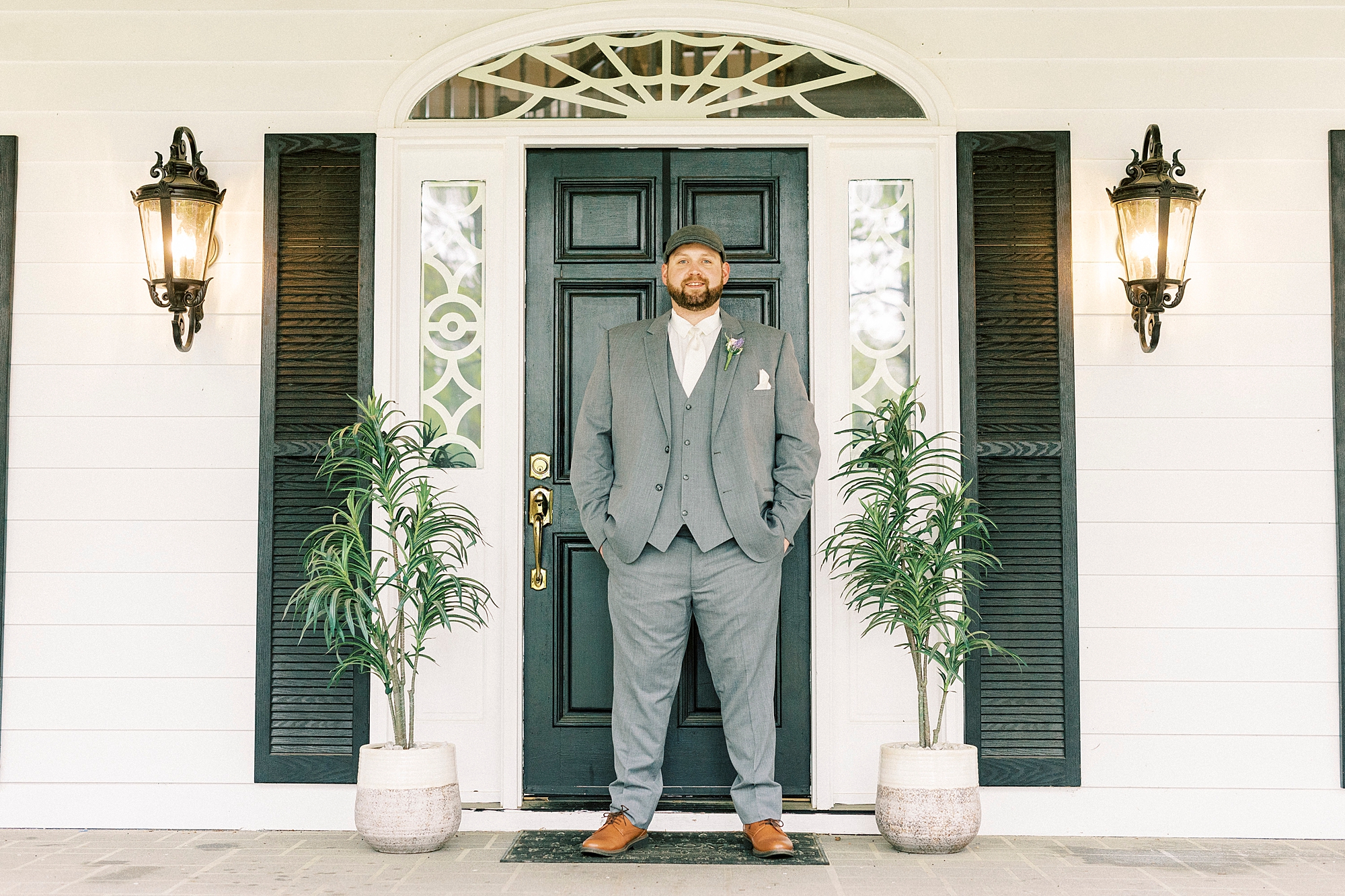groom stands with hands in pocket of grey suit by green door at The Saratoga Springs