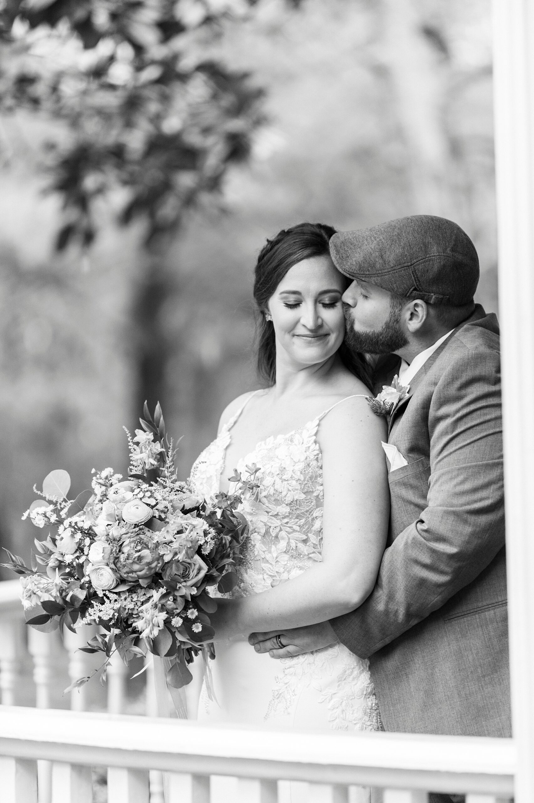 groom kisses bride's cheek standing on porch at The Saratoga Springs