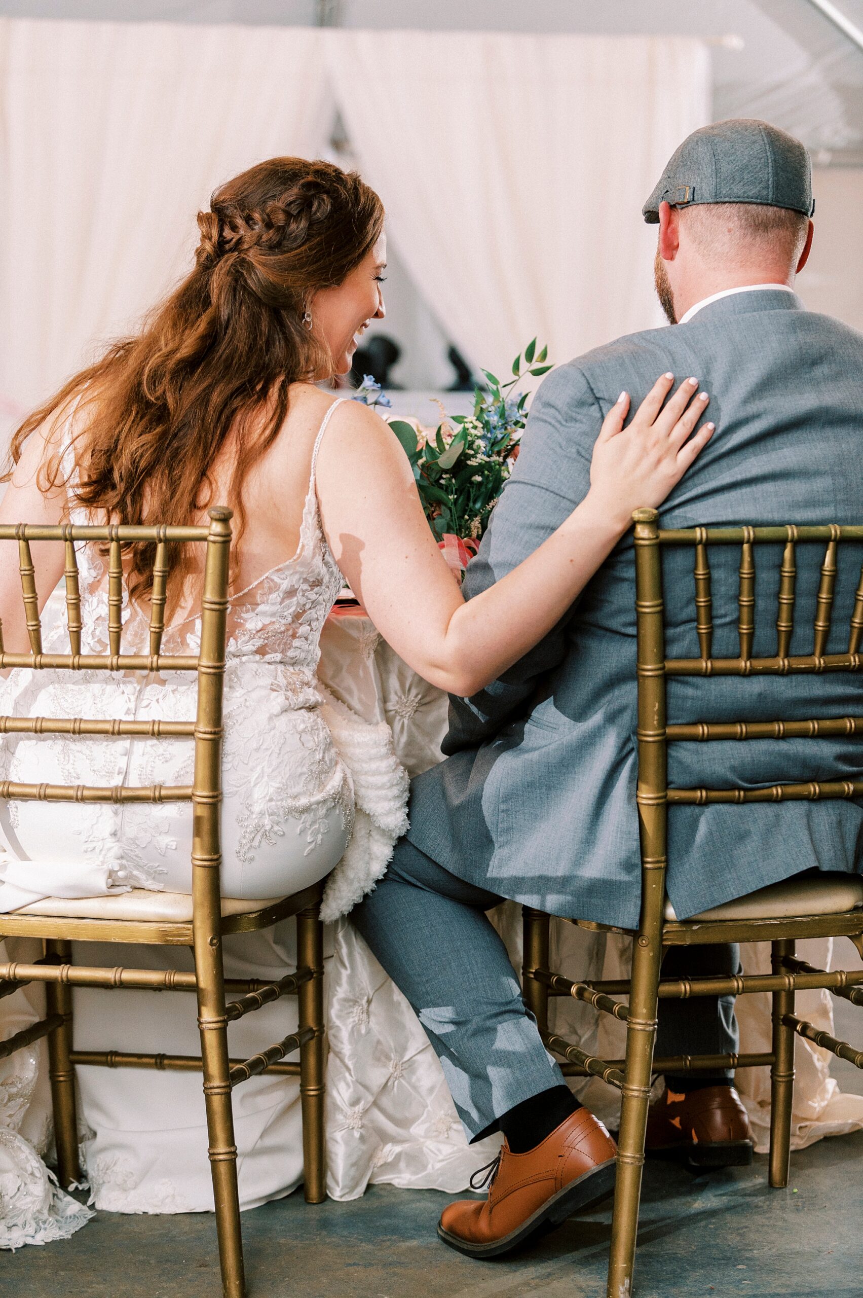 bride and groom sit at sweetheart table holding each other's shoulders 