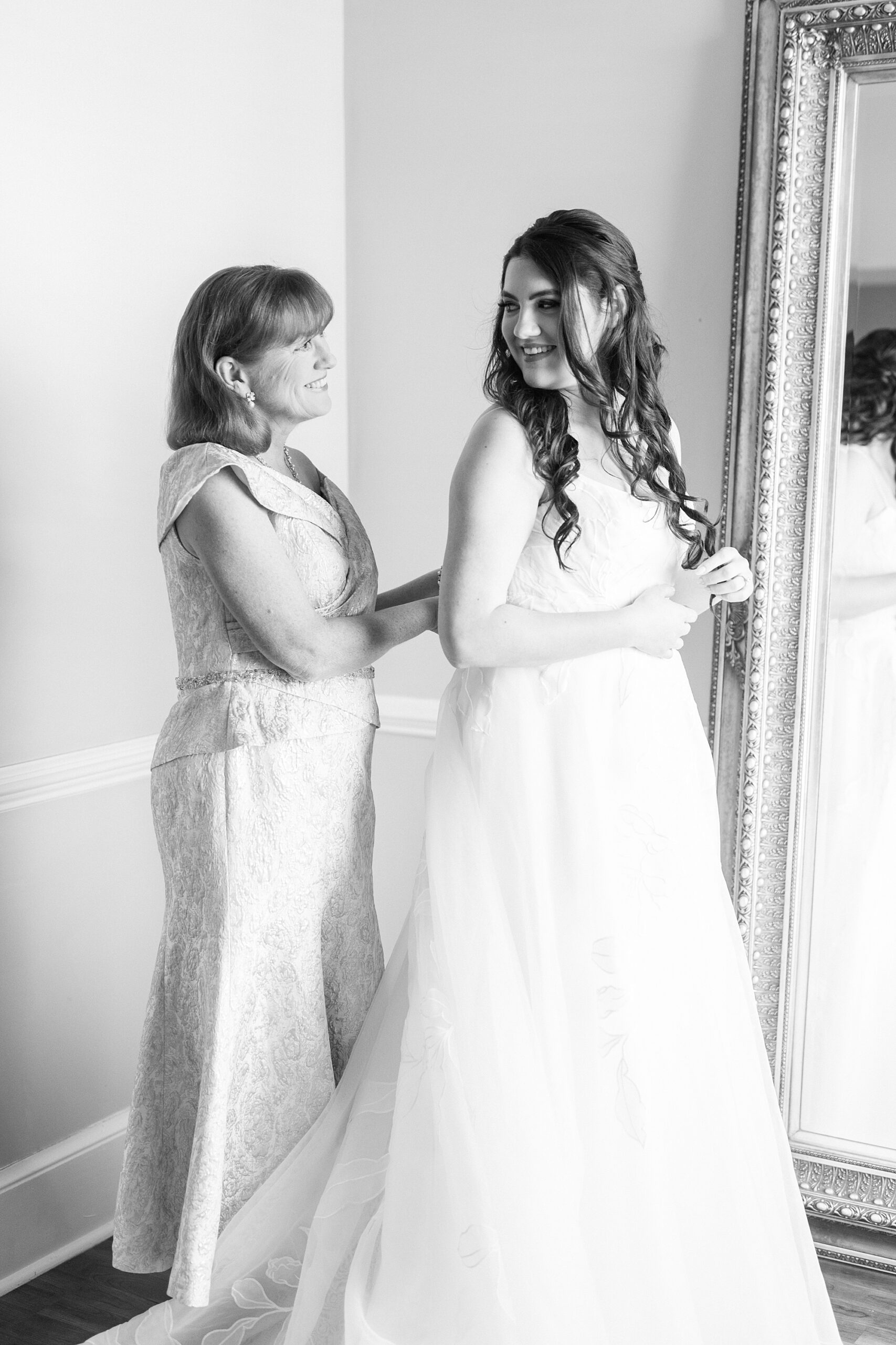 mother buttons up wedding dress for bride 