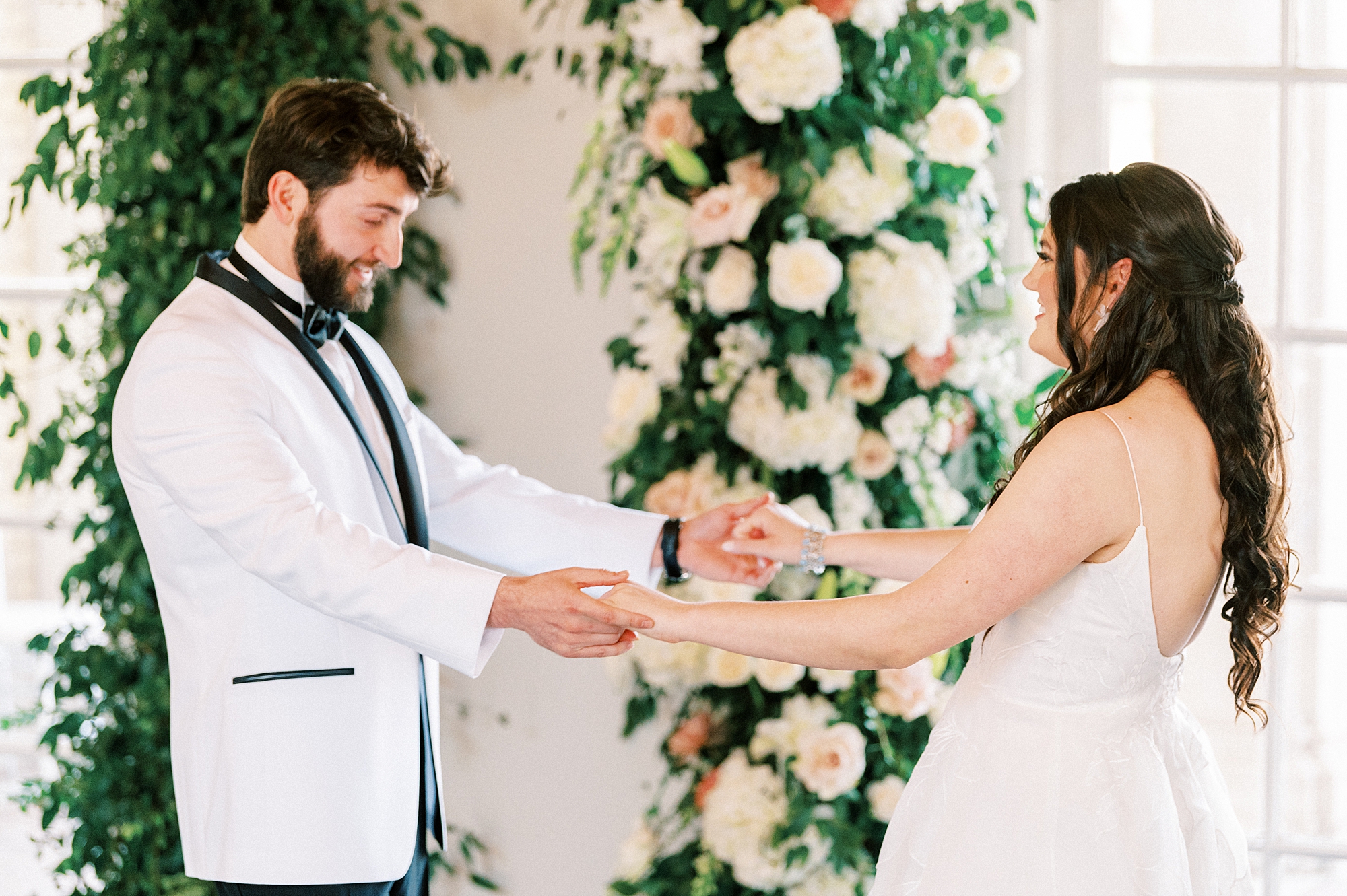 bride and groom hold hands while groom looks down at bride's wedding dress 