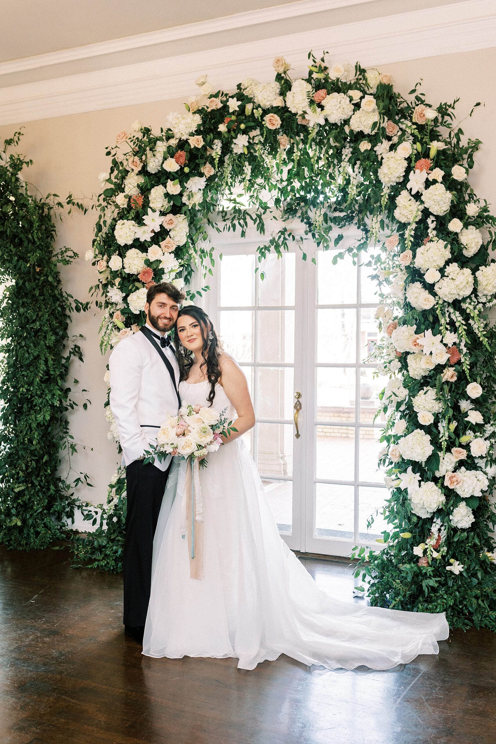 bride leans head on groom's chest under rose arbor inside Separk Mansion