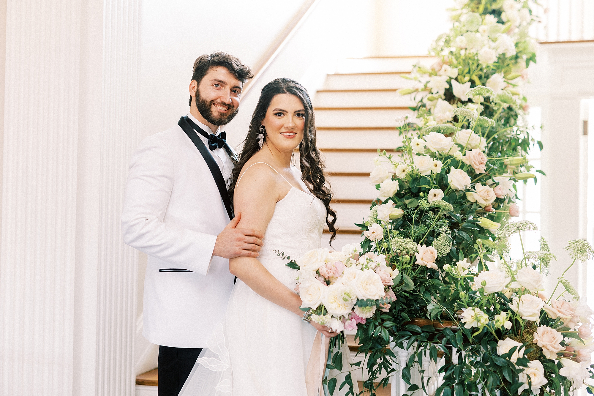 groom in white tux jacket holds bride's arm standing at staircase inside Separk Mansion