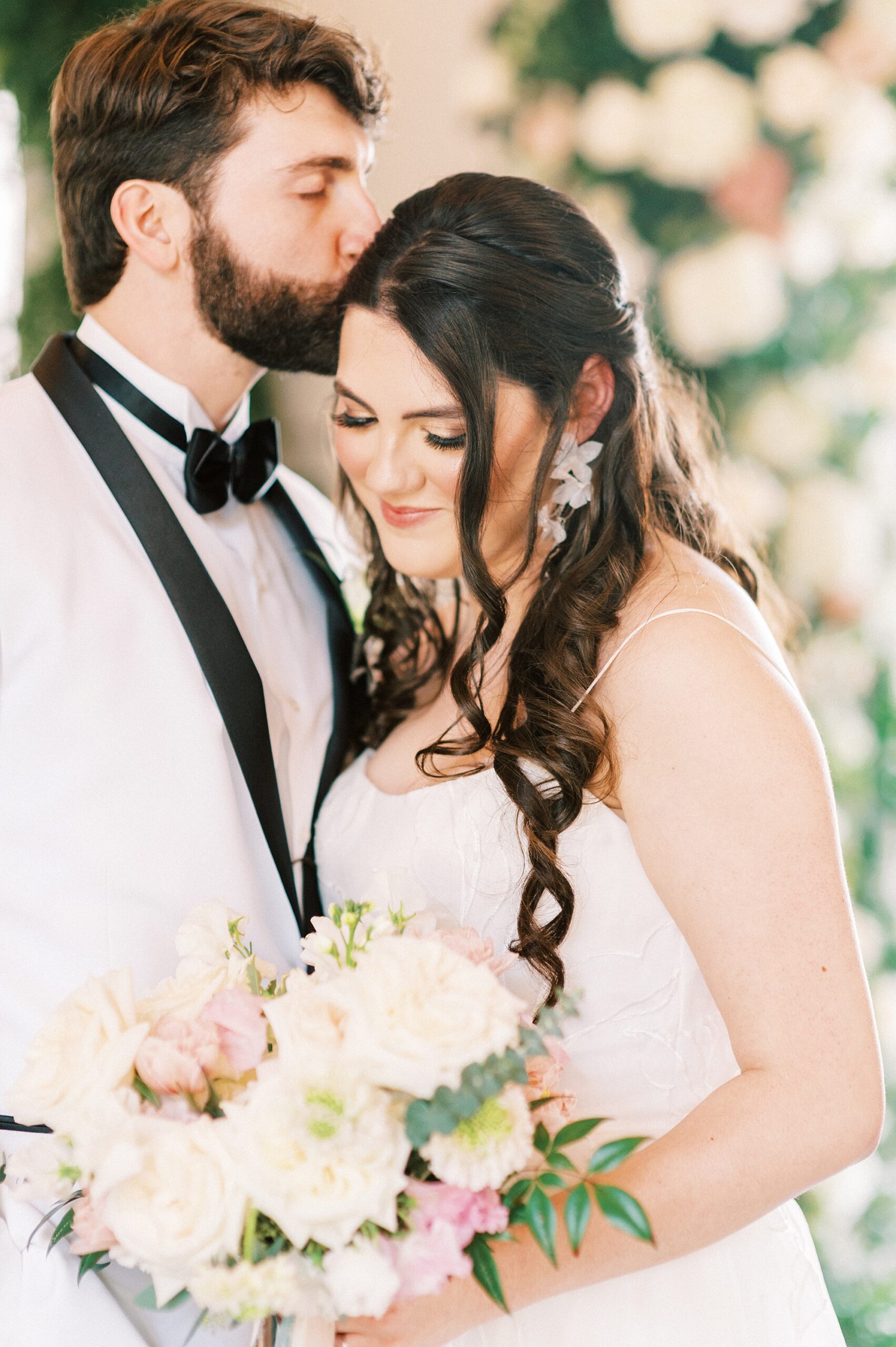groom in white jacket kisses bride's forehead during NC wedding photos 