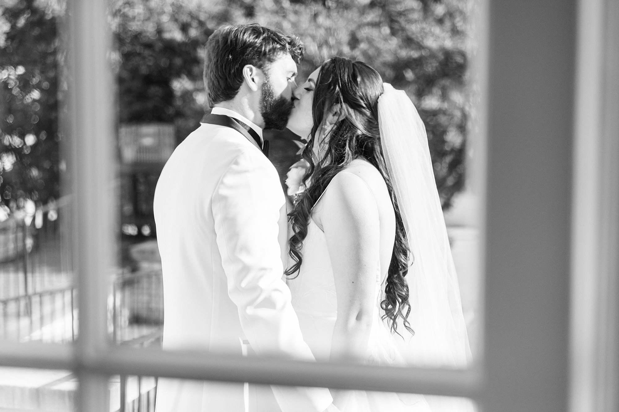 bride and groom kiss behind window pane 