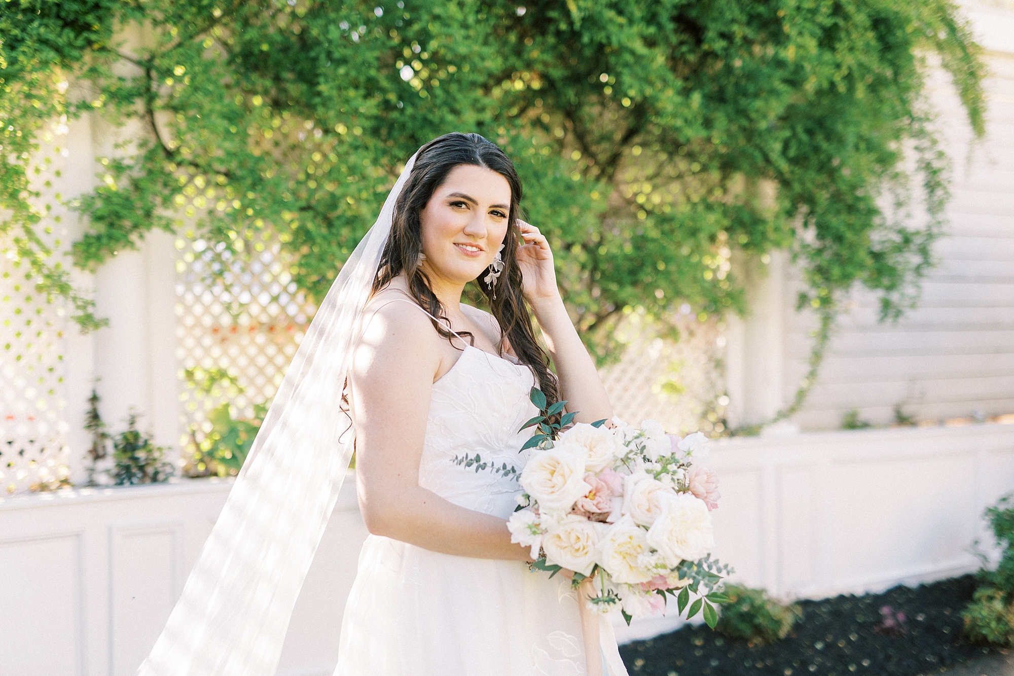bride smiles pushing hair behind ear while veil drags behind her 