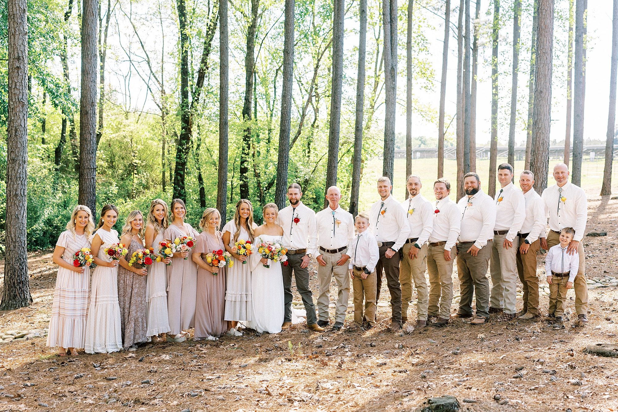 bride and groom stand with wedding party on lawn of home