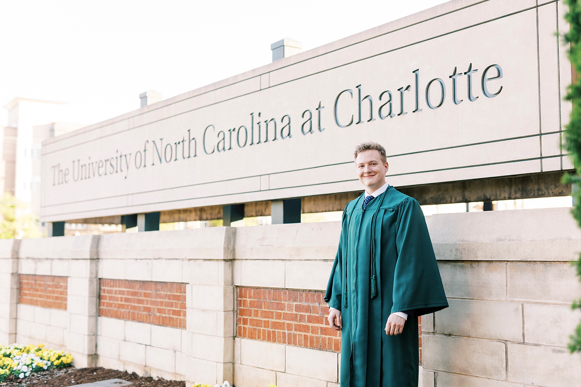 graduating senior poses in green gown near University of North Carolina at Charlotte sign
