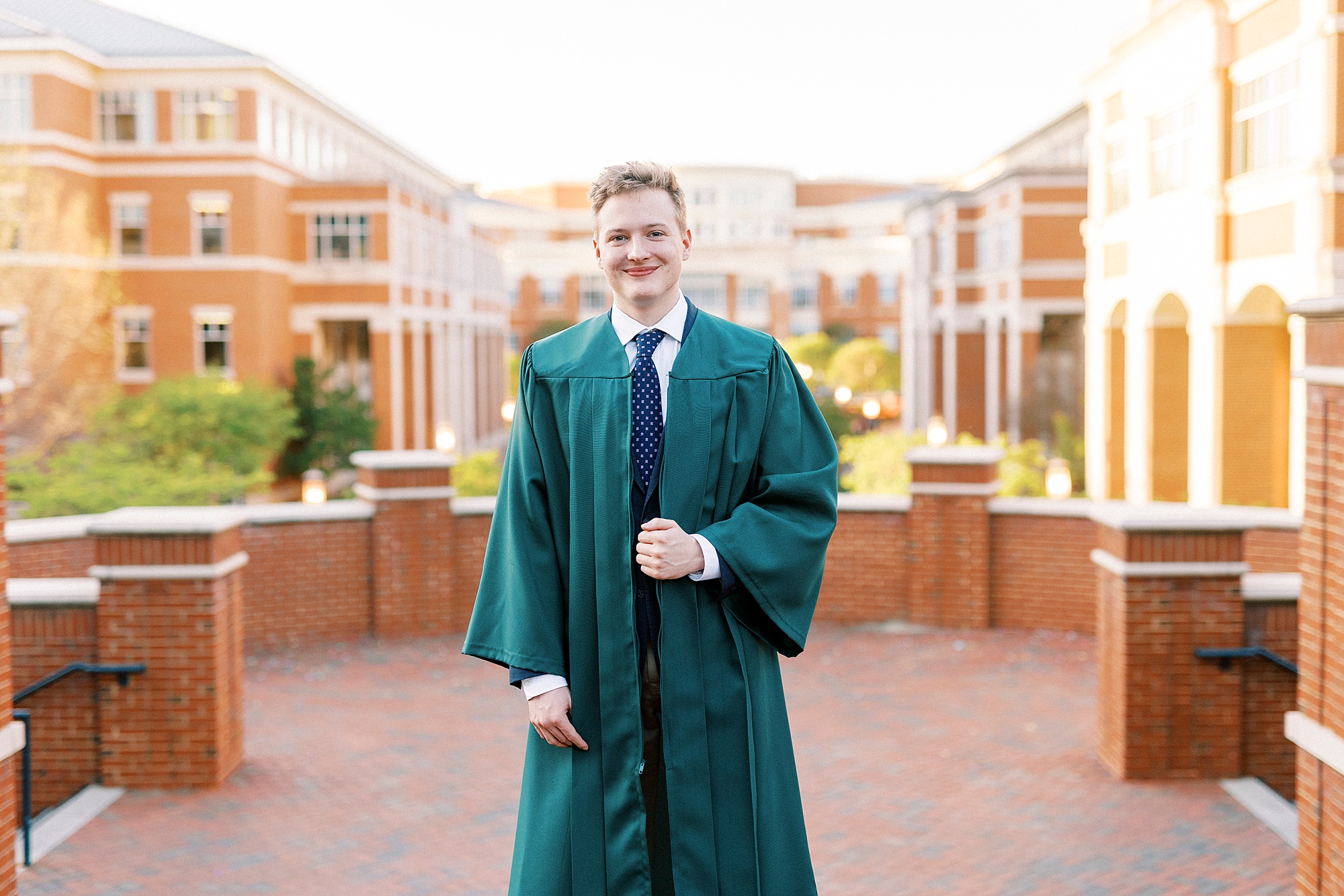 groom stands with with hands on lapels of graduation gown