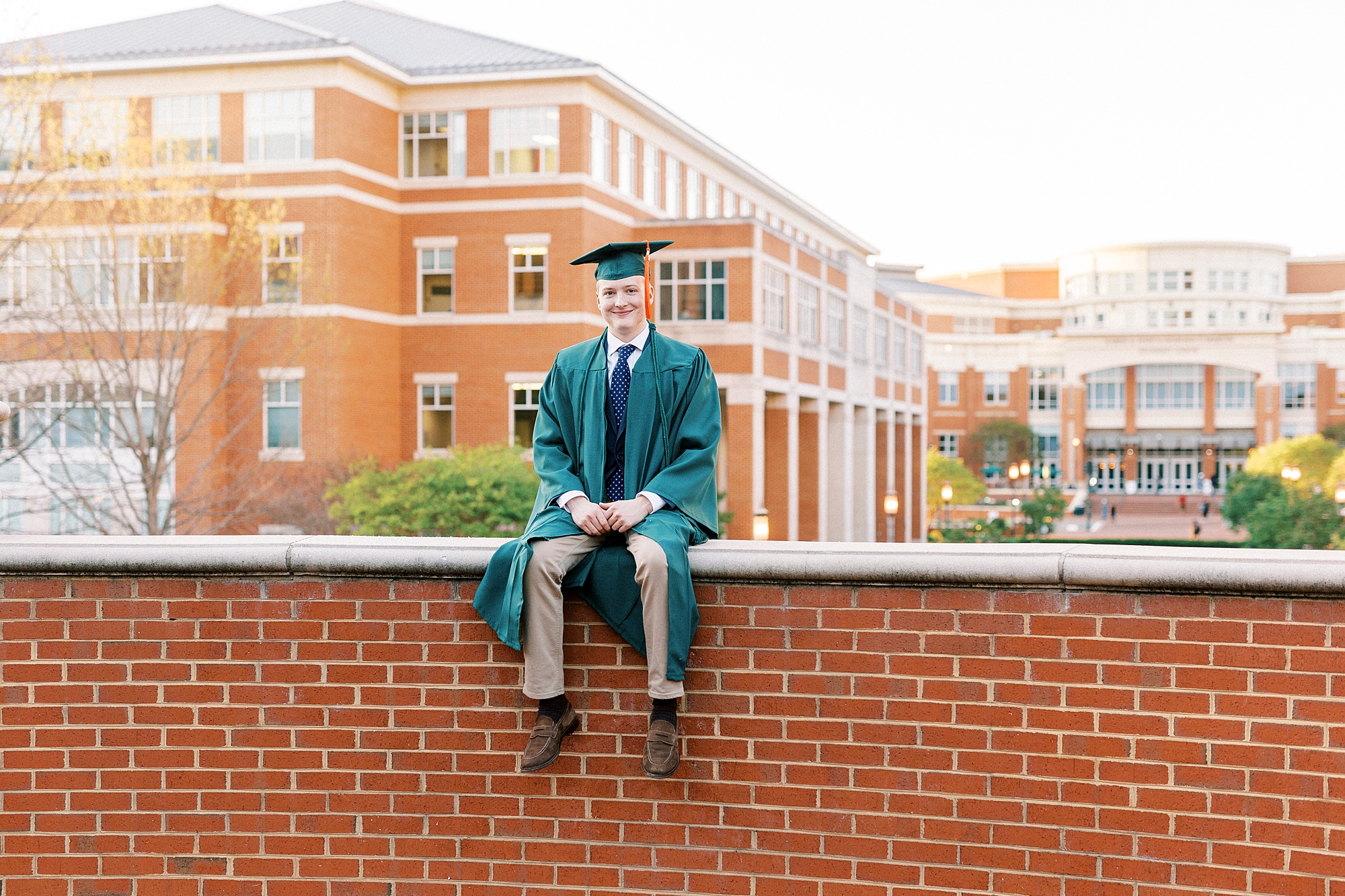 graduating male sits on brick wall in Charlotte NC