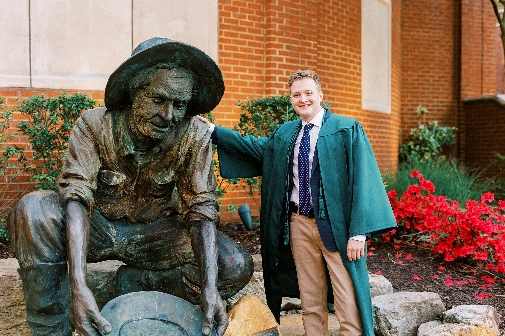 senior guy leans against statue during UNC Charlotte senior portraits