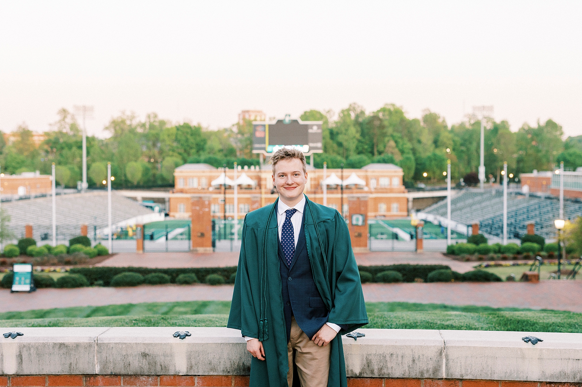 senior sits on brick wall looking at football field at UNC Charlotte